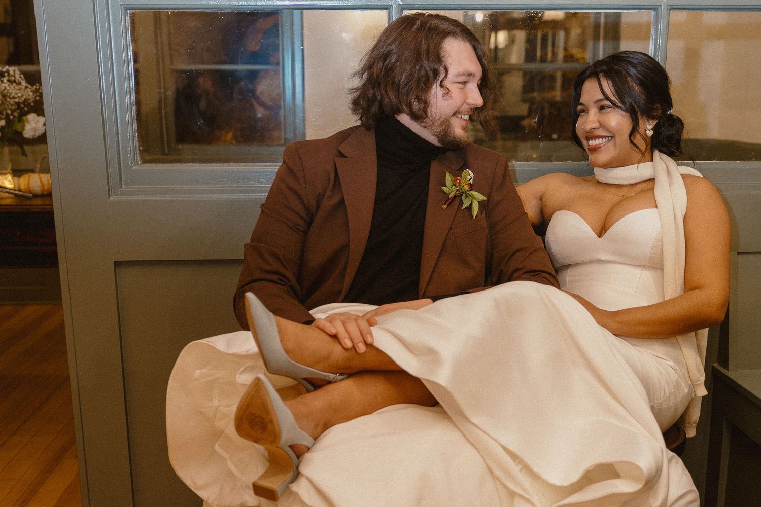 Bride and groom laughing together, groom in brown suit holding bride in white gown.