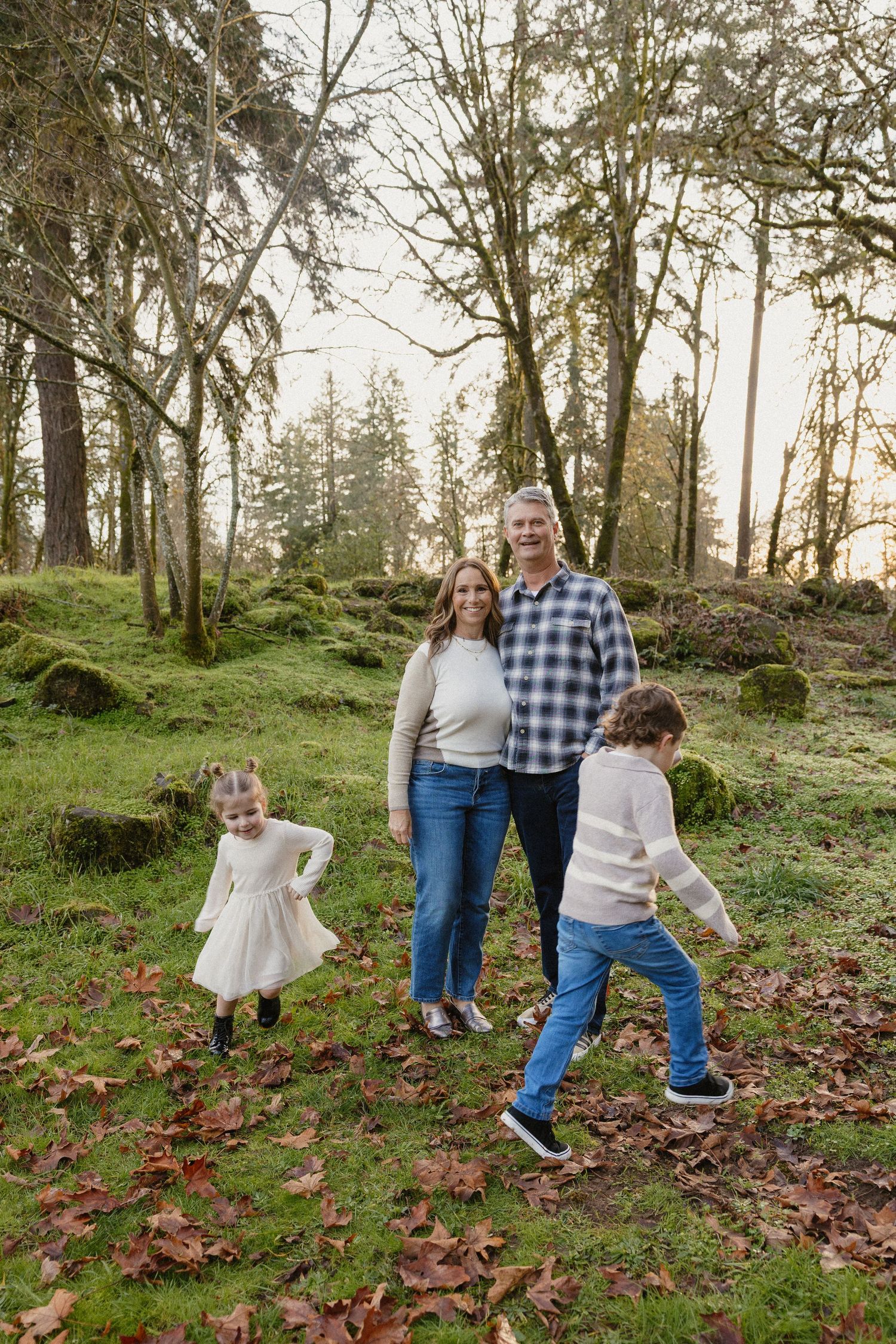 Smiling couple with two young children playing in moss-covered autumn woodland park.