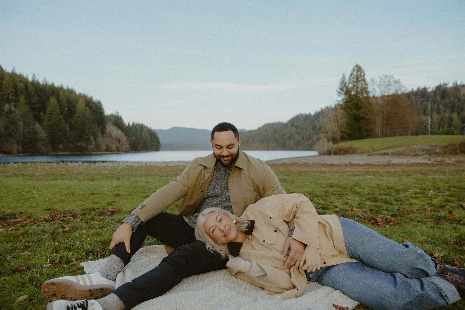 Couple relaxing on blanket by lake, woman lying on mans lap smiling outdoors.