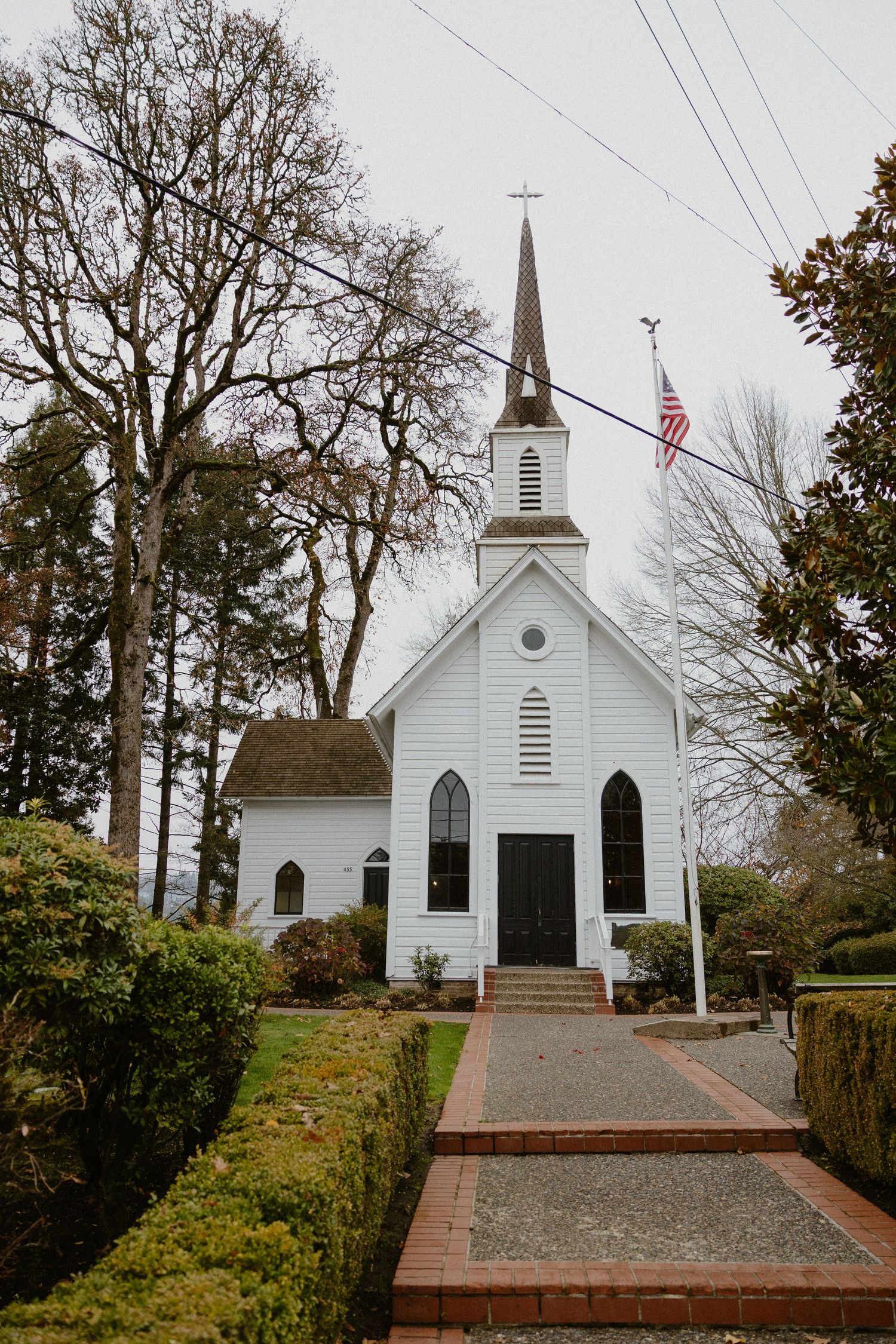 Classic white wooden chapel with steeple and American flag on overcast day.