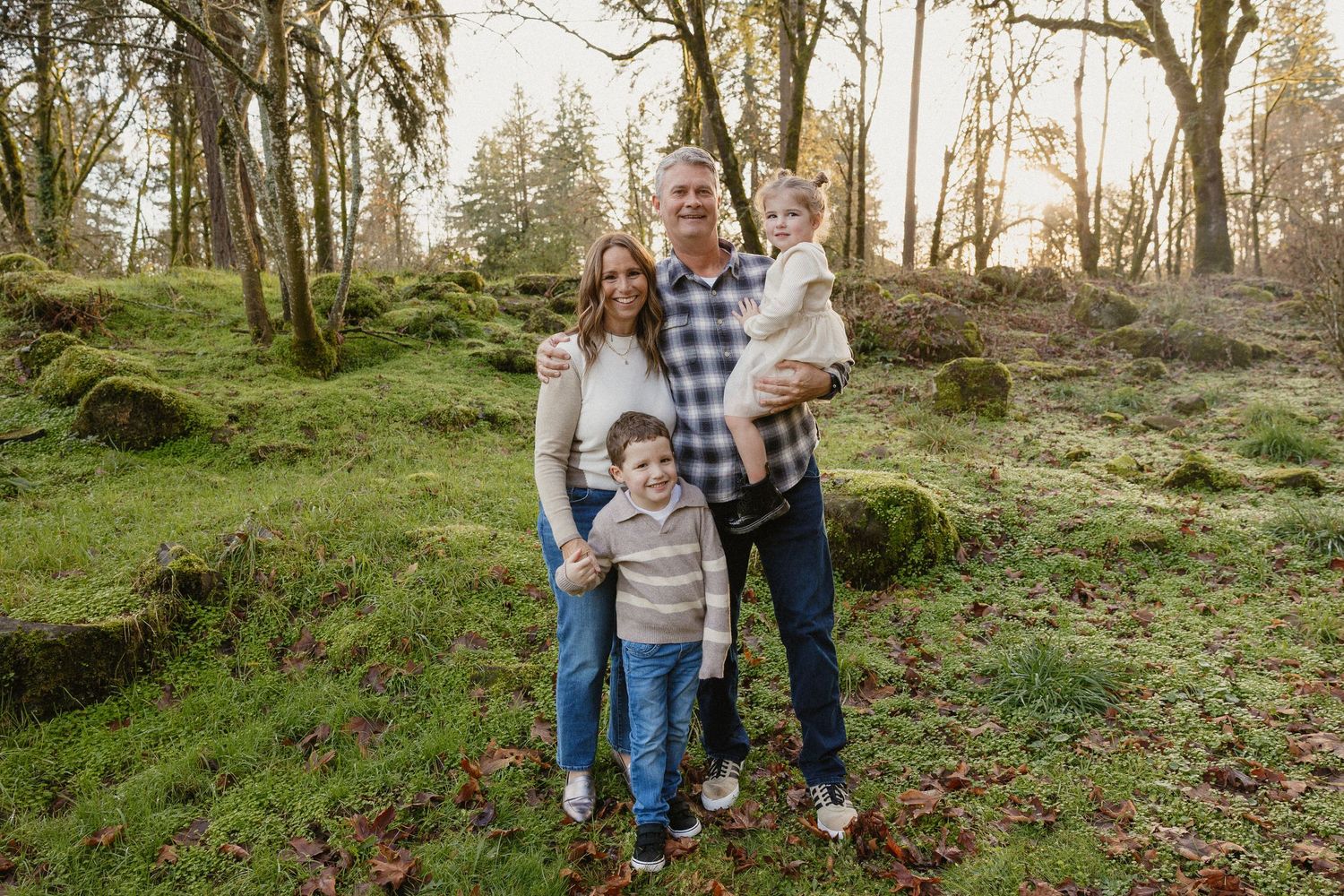 Happy family of four posing together in mossy woodland forest during golden hour.