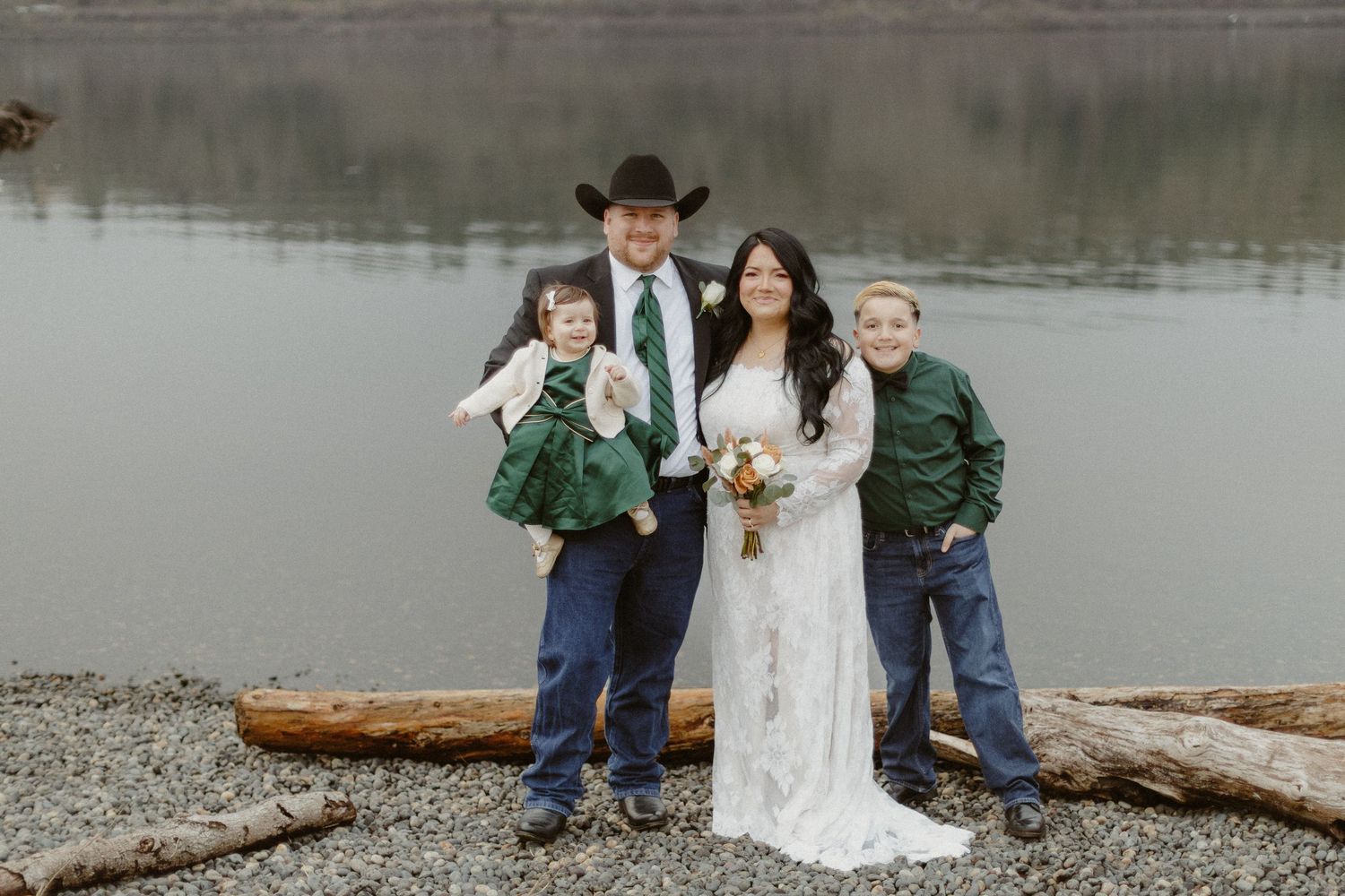 Wedding family portrait with bride, groom in cowboy hat, and two children by a misty lakeside.