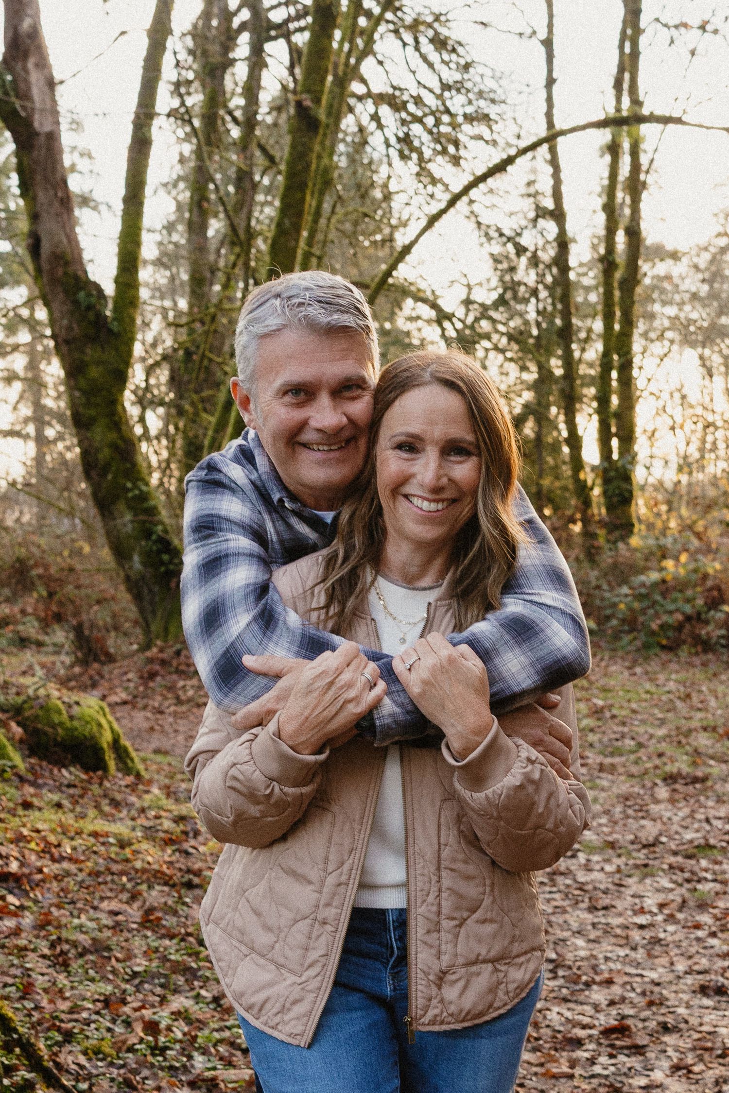 Happy couple embracing warmly in autumn woodland forest with moss-covered trees.
