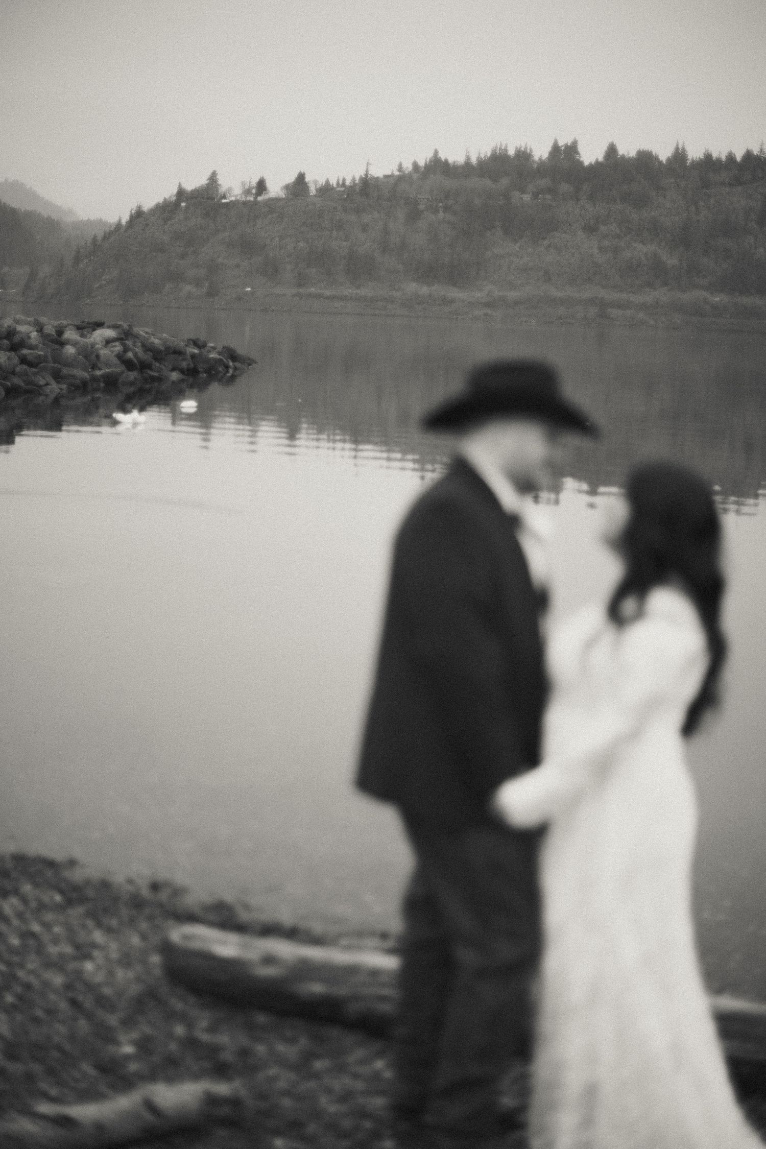Black and white photo of wedding couple sharing intimate moment by a reflective lake shoreline.