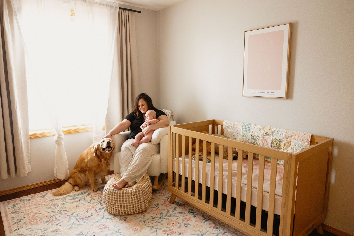 Mother relaxing in nursery chair with newborn baby and golden retriever beside wooden crib.
