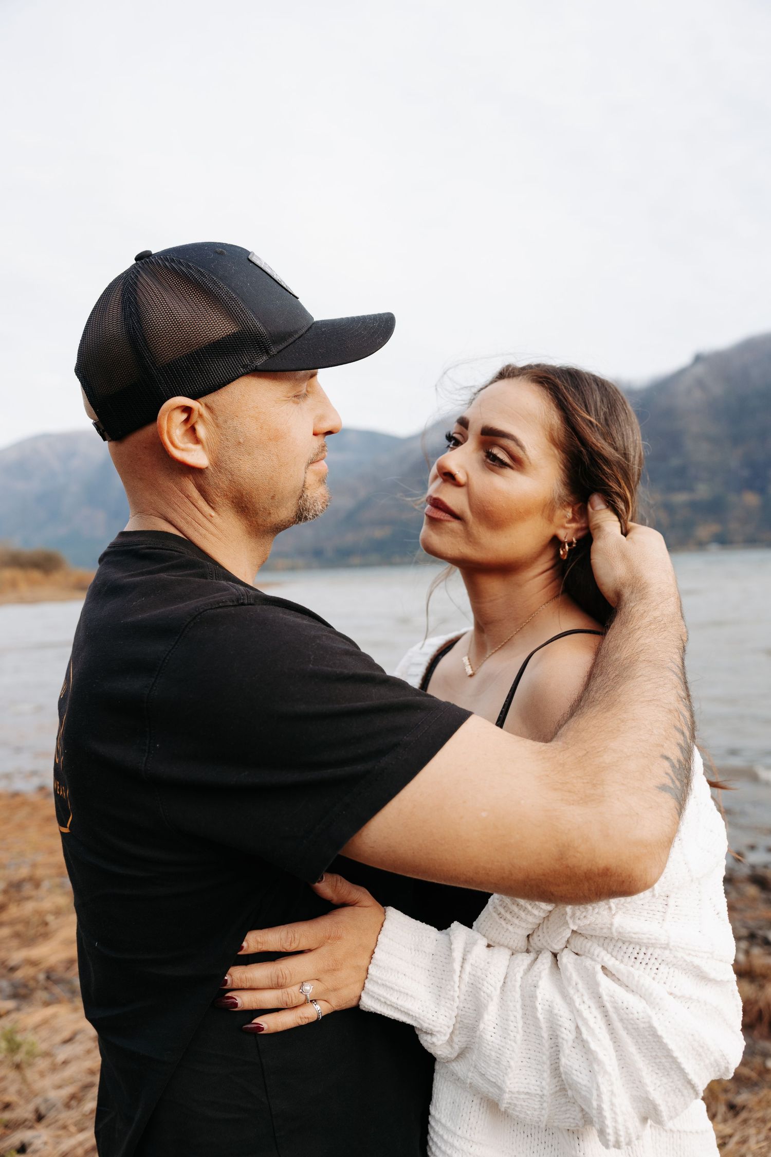 Couple embracing intimately by a mountain lake with woman gazing up at her partner.