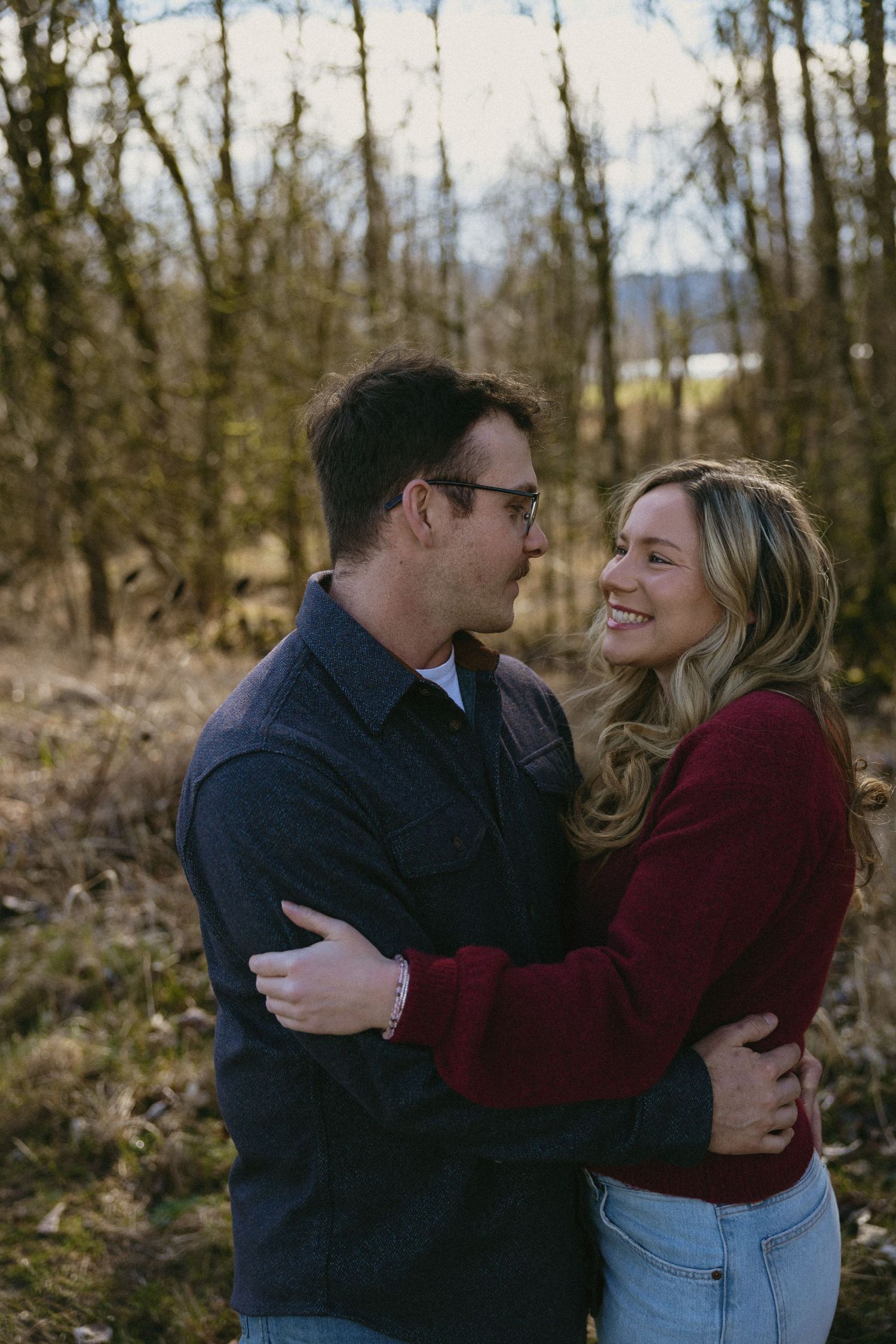 Happy couple hugging and smiling at each other in a natural wooded outdoor setting.