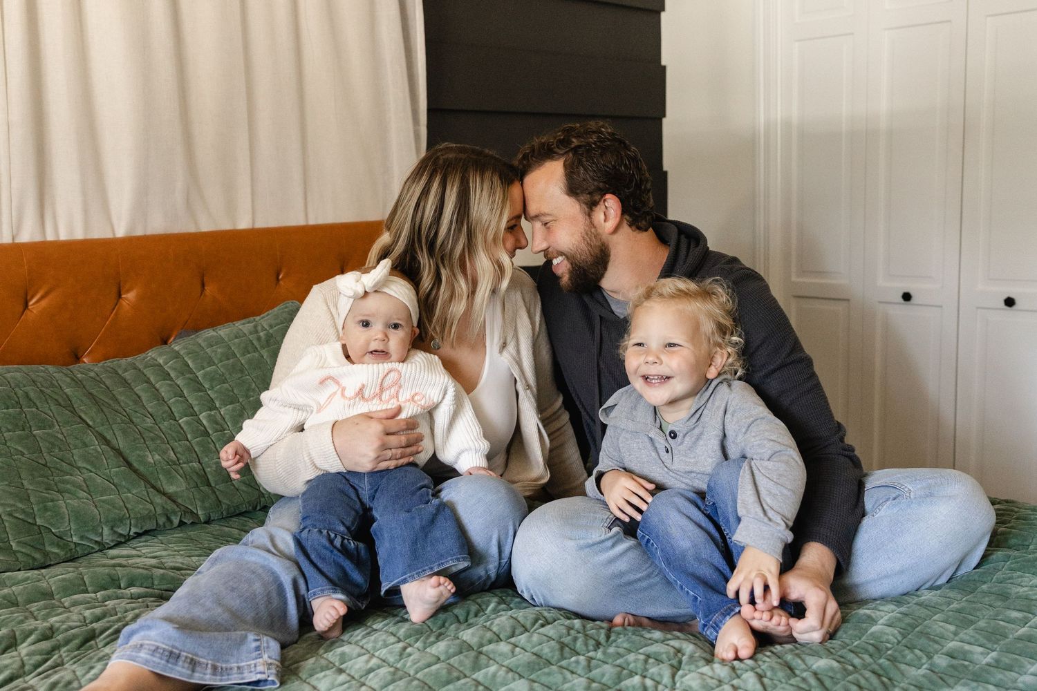 Happy family of four with two young children sharing a joyful moment on a cozy bed.