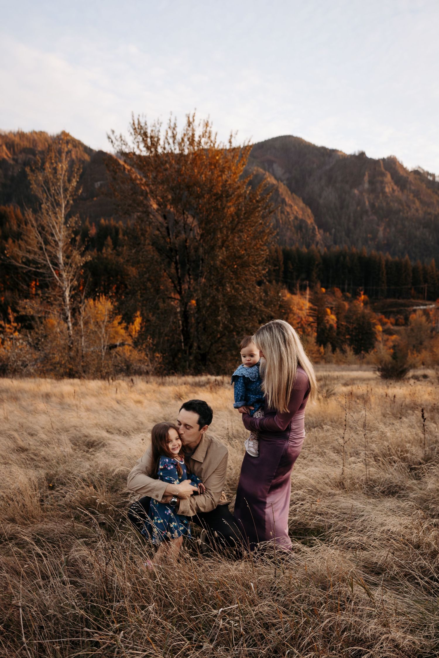 A family of four enjoys a warm autumn moment together in a mountain meadow at sunset.