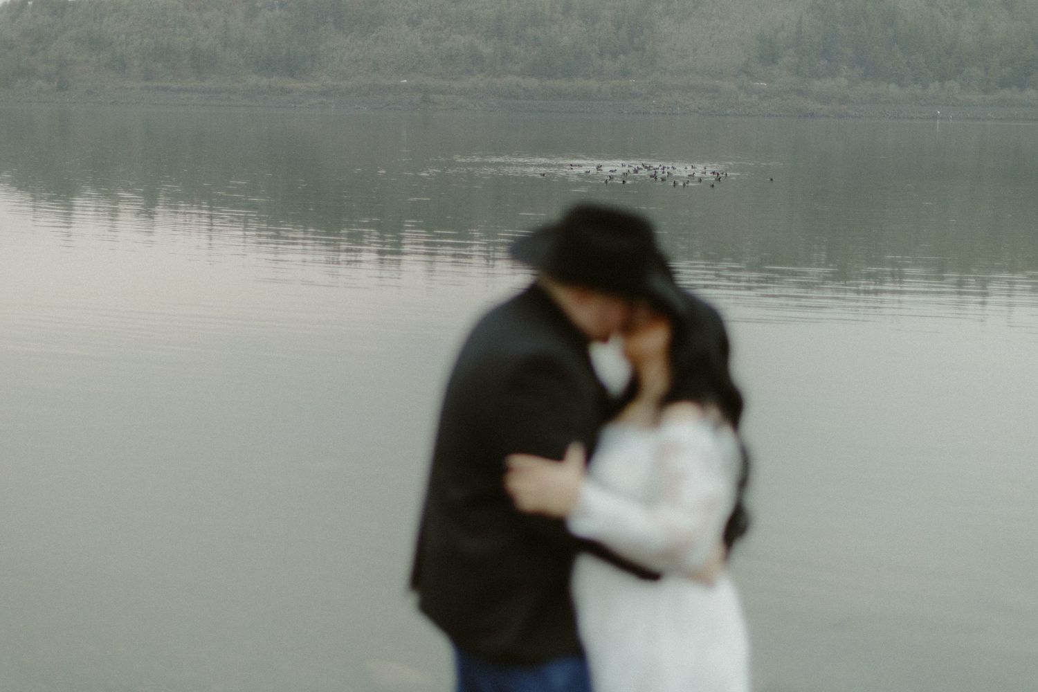 A blurred romantic couple shares an intimate moment by a calm lakeside.