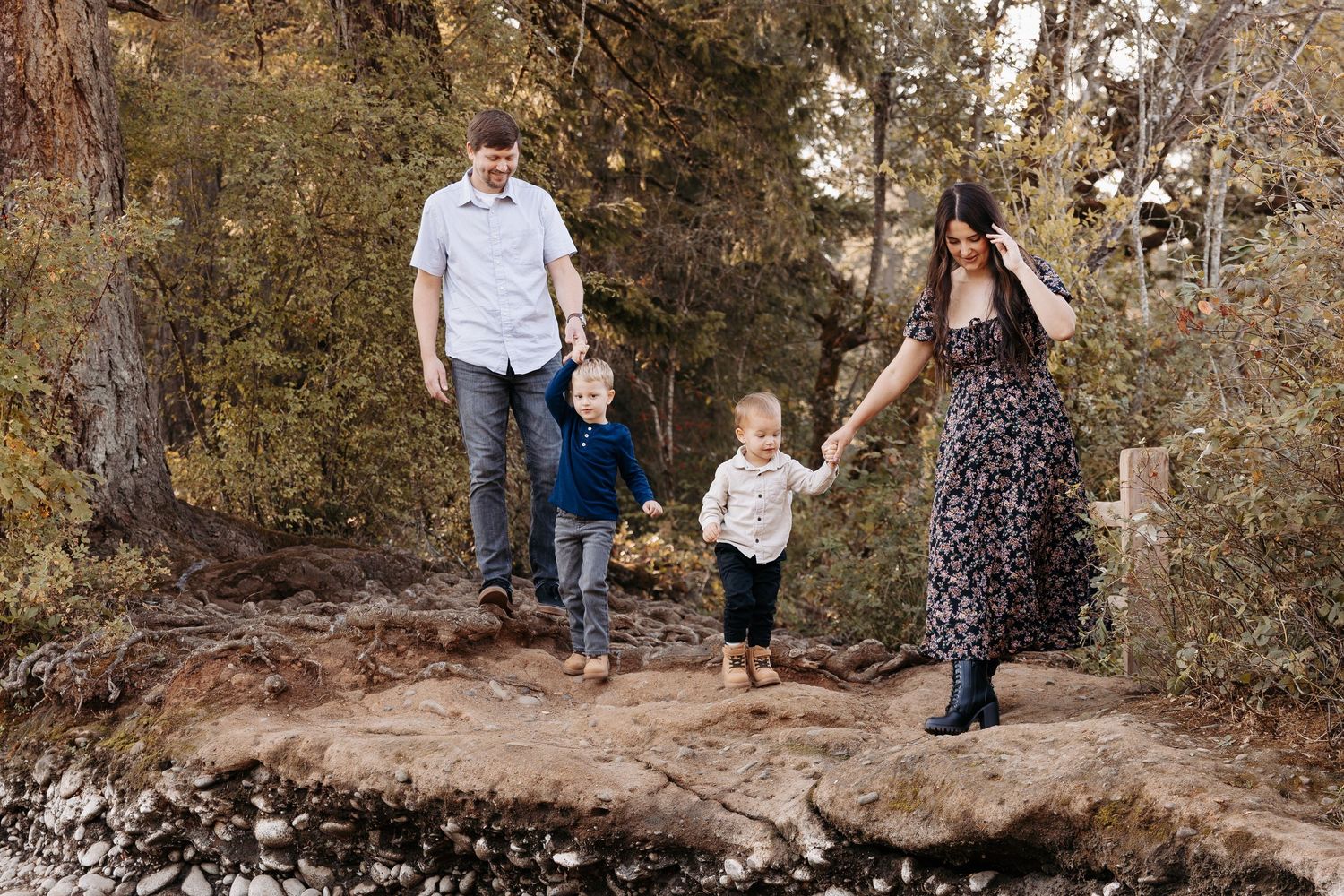 Family walking hand-in-hand on rocky path through autumn forest with two young children.