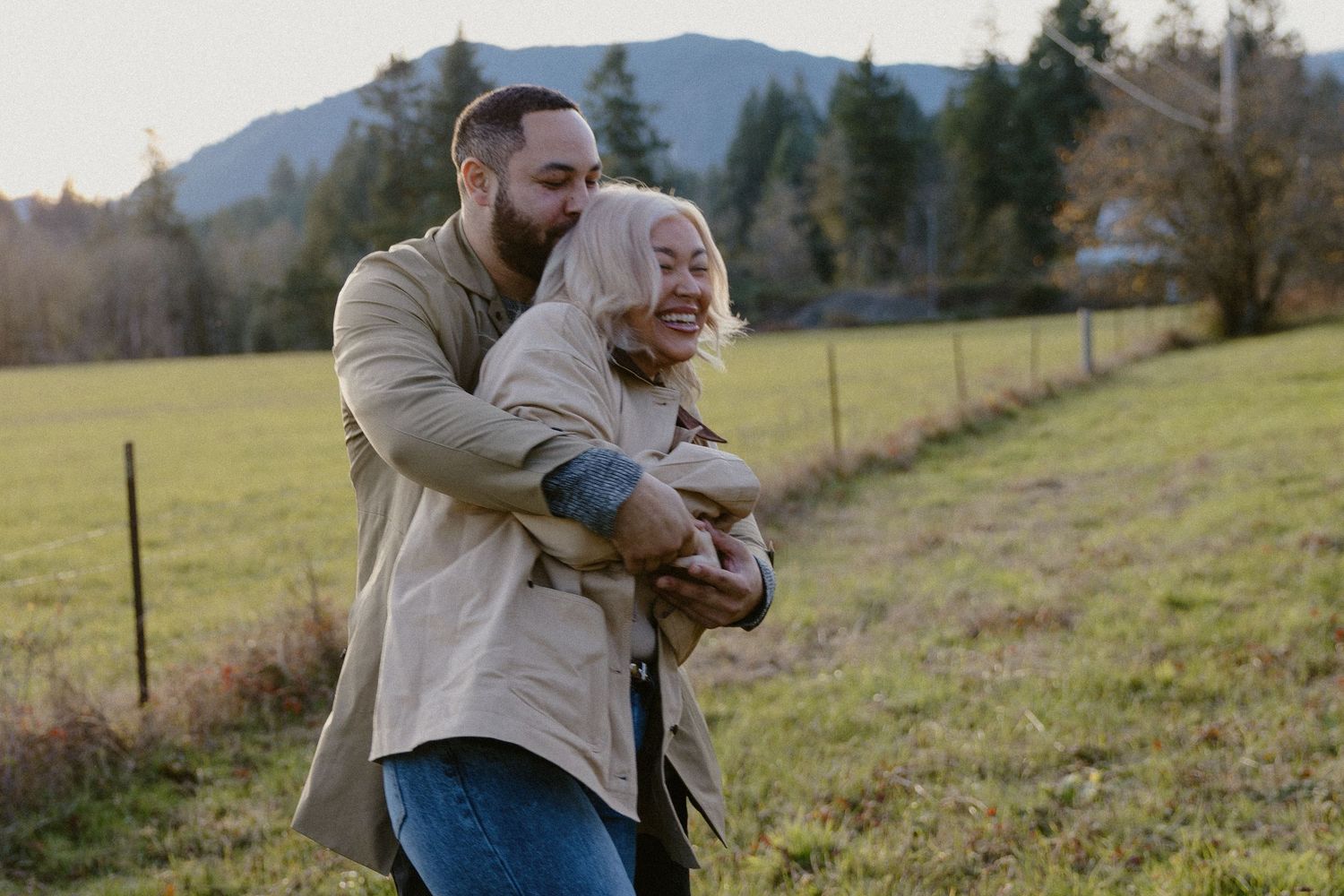 Man playfully hugging woman from behind in a grassy field at sunset.