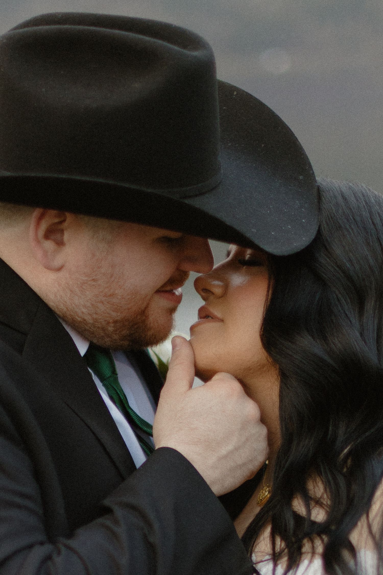 Intimate close-up of groom in black cowboy hat tenderly touching bride's chin before a kiss.
