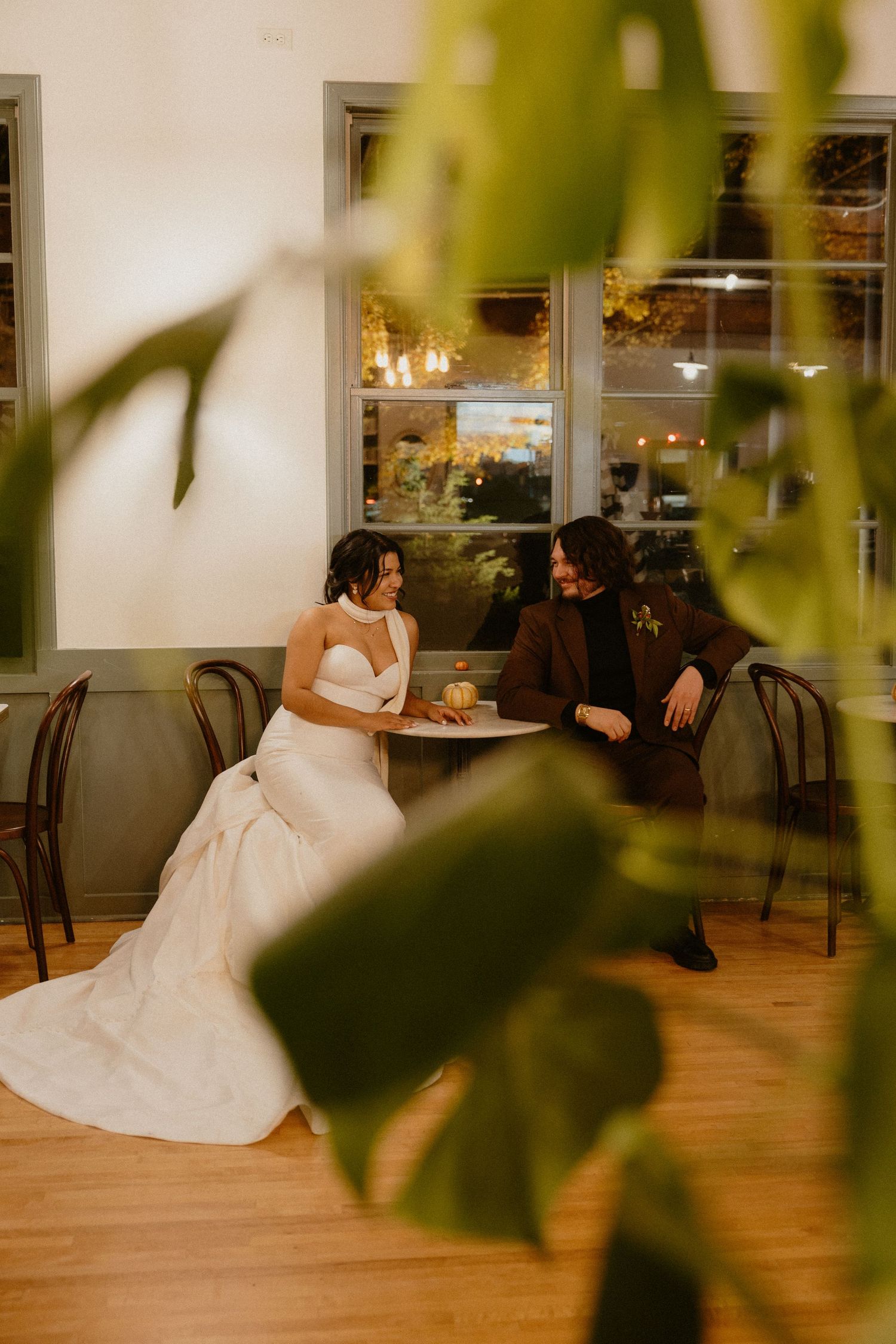Bride and groom share an intimate moment seated at a table in a warmly lit wedding venue.