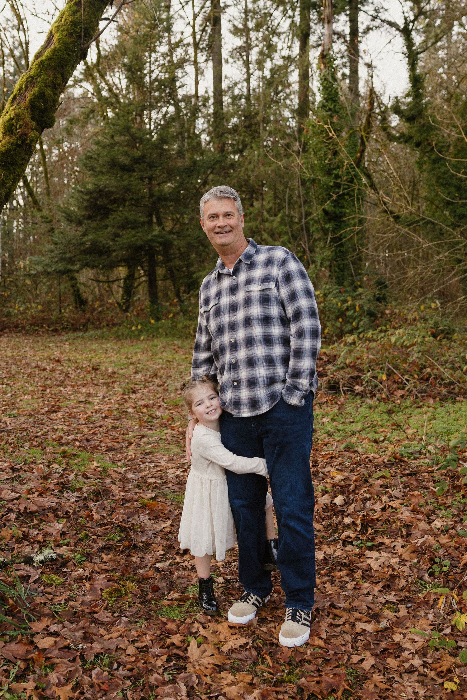 Smiling grandfather in plaid shirt hugging young girl in autumn forest setting.