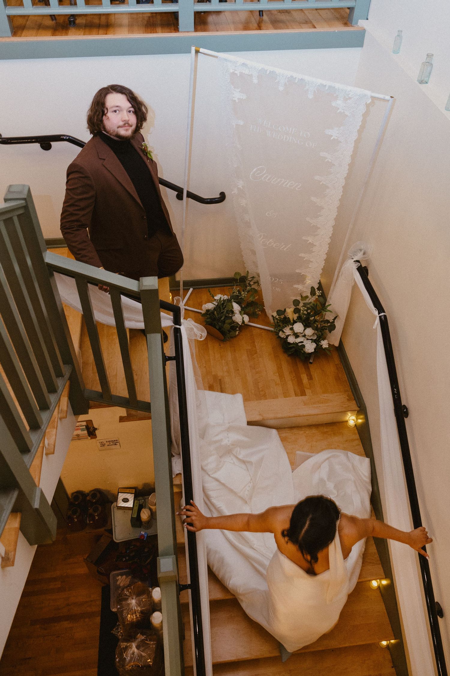 Overhead view of groom in brown suit and bride in white gown on staircase.