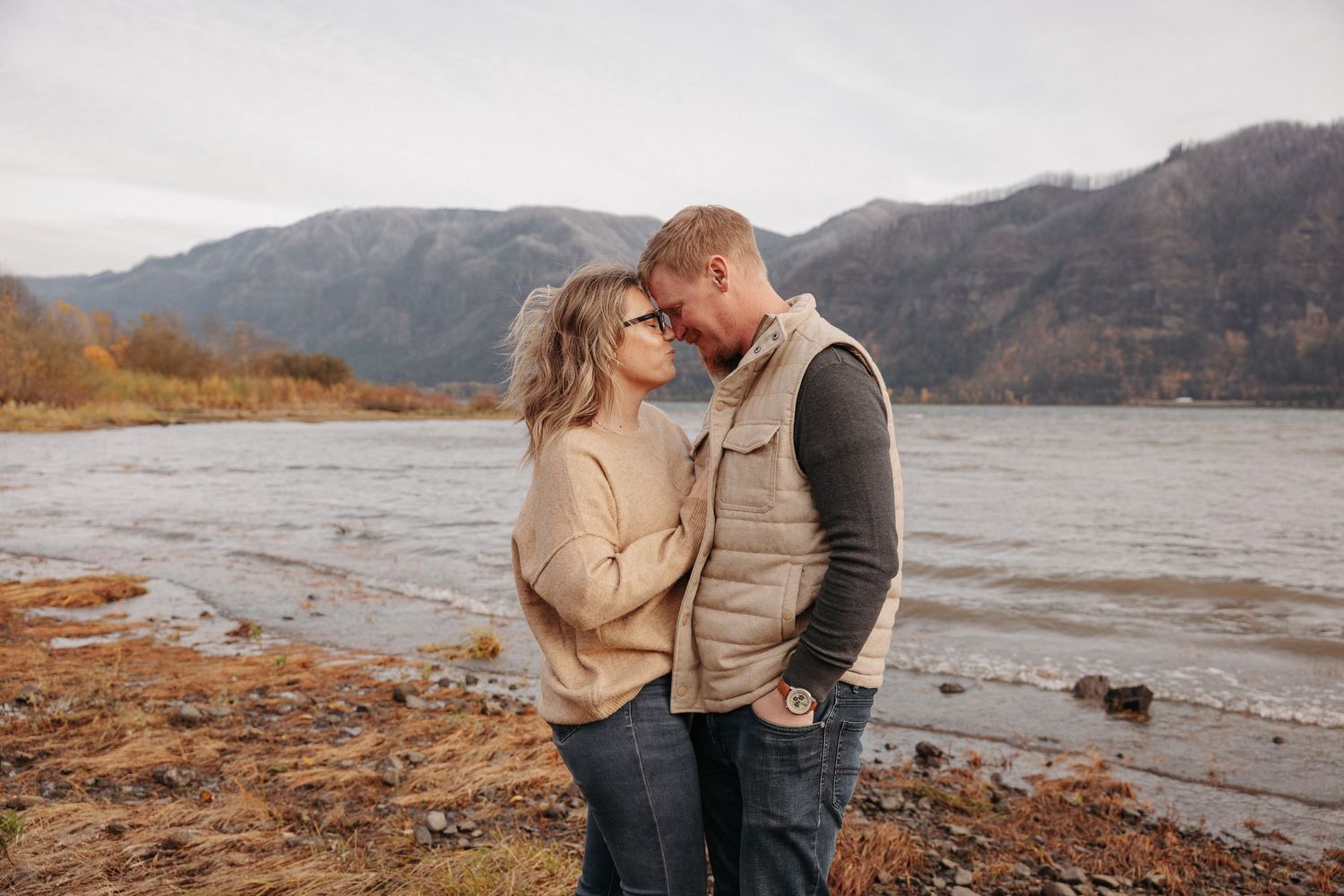 Couple sharing a romantic kiss by a mountain lake on a cloudy autumn day.