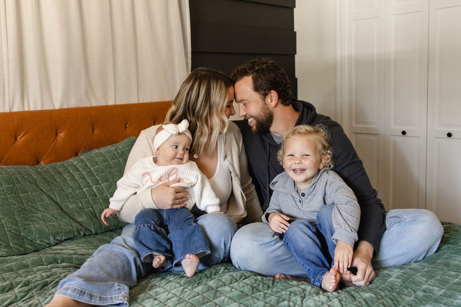 Happy family of four sharing tender moment together on green bed at home.
