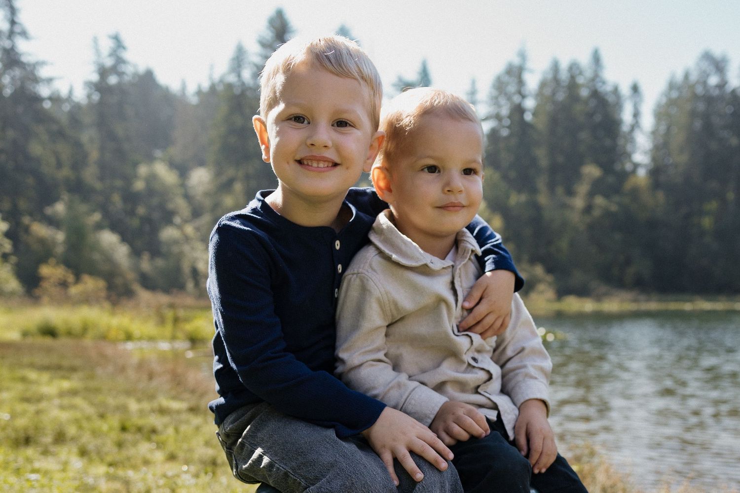 Two young brothers smiling together by a sunny lakeside.
