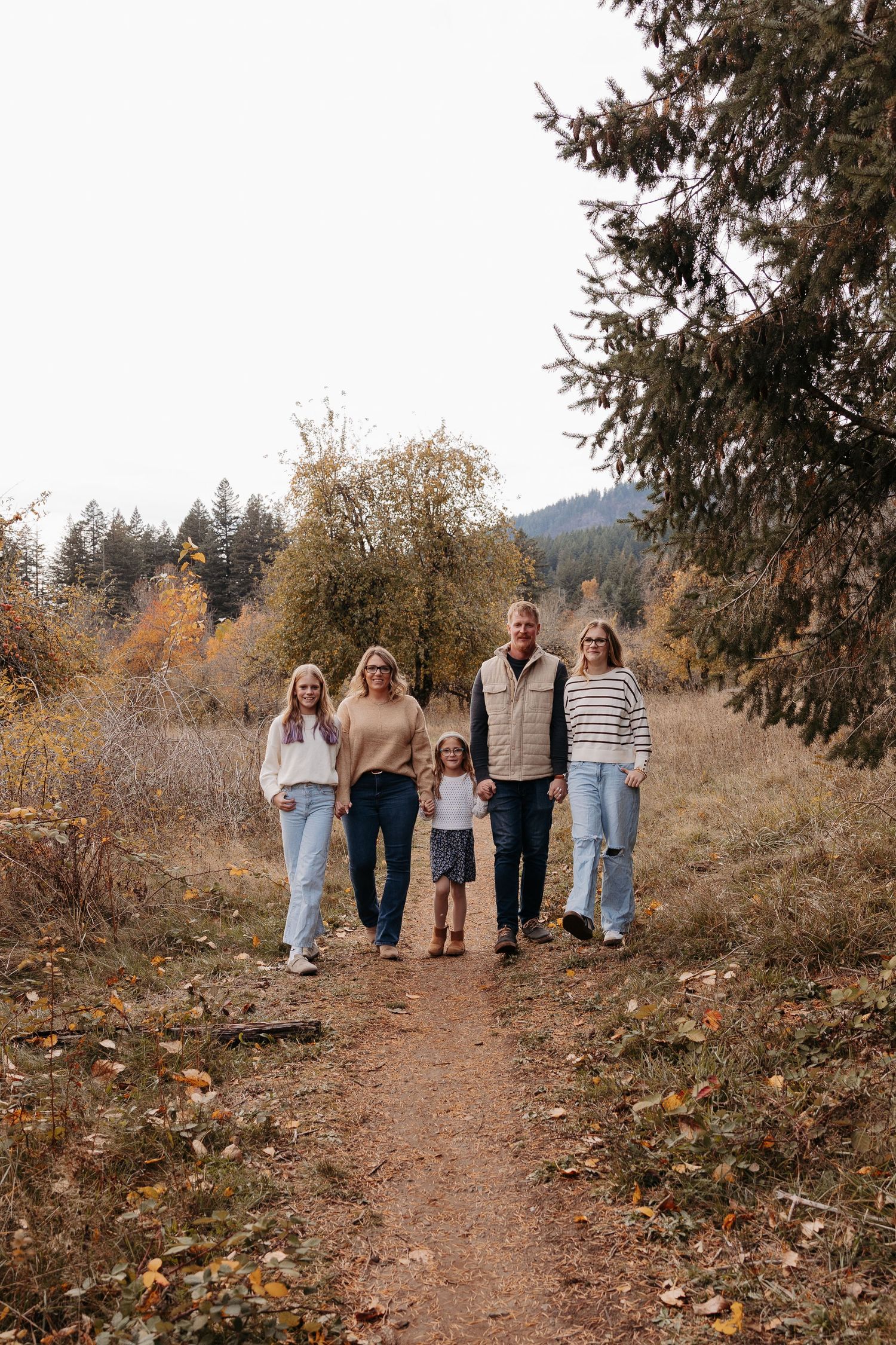 Family of five walking together on an autumn trail surrounded by fall foliage.