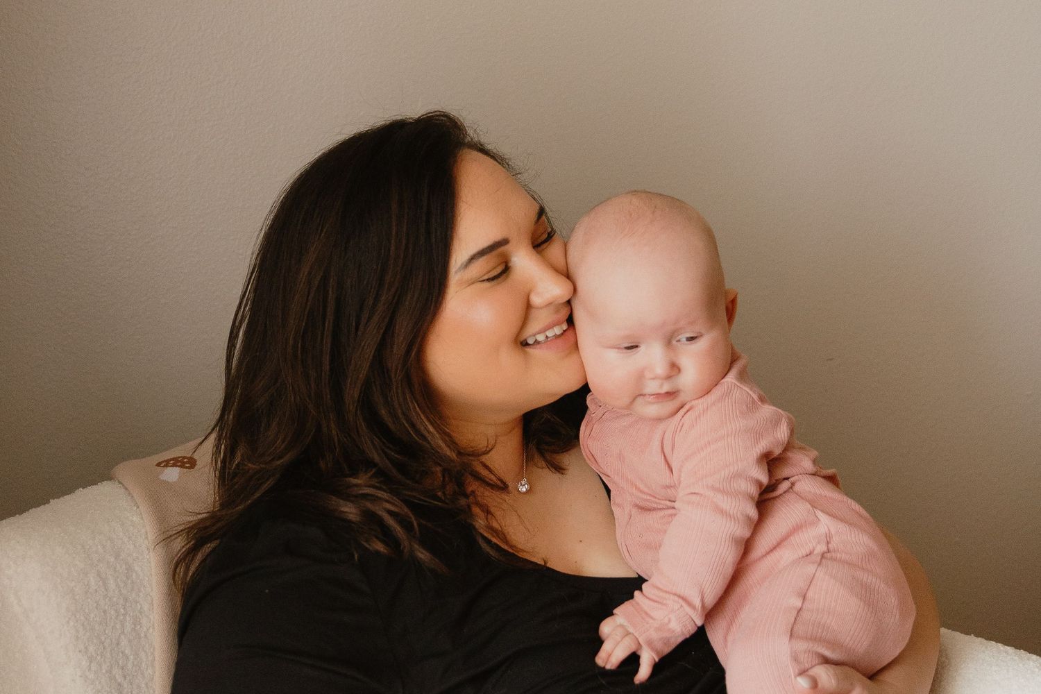 Loving mother smiling and cuddling her infant dressed in pink onesie indoors.