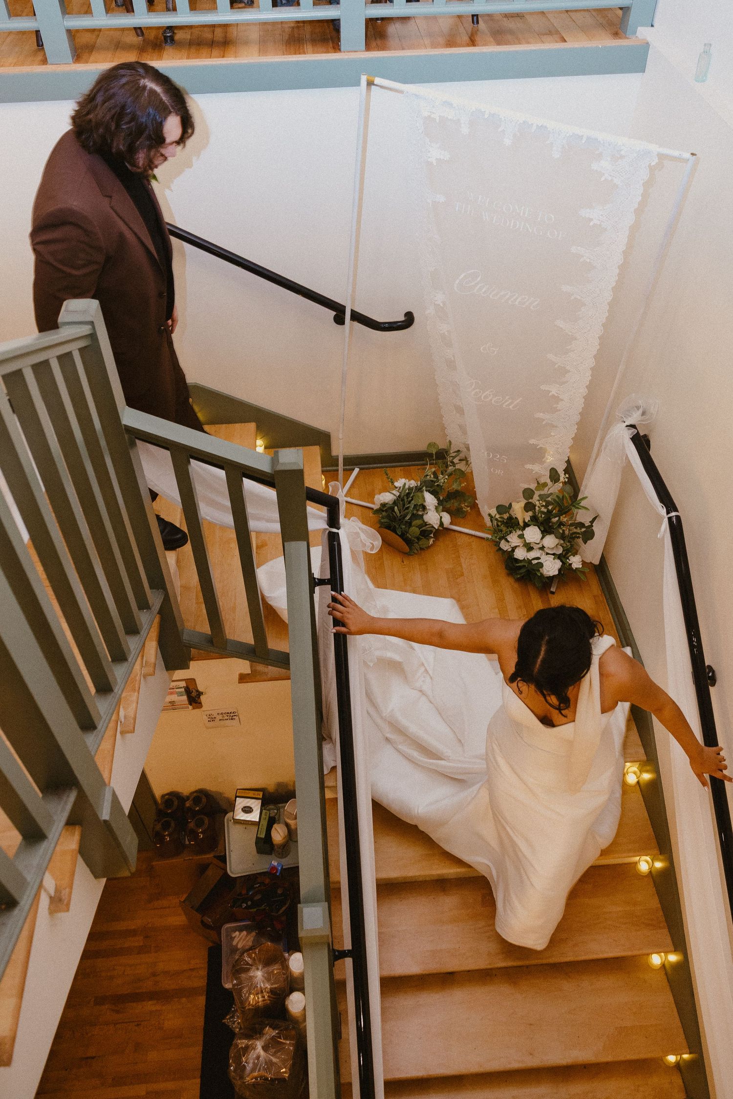 Aerial view of bride in white gown and groom on wooden staircase at venue.