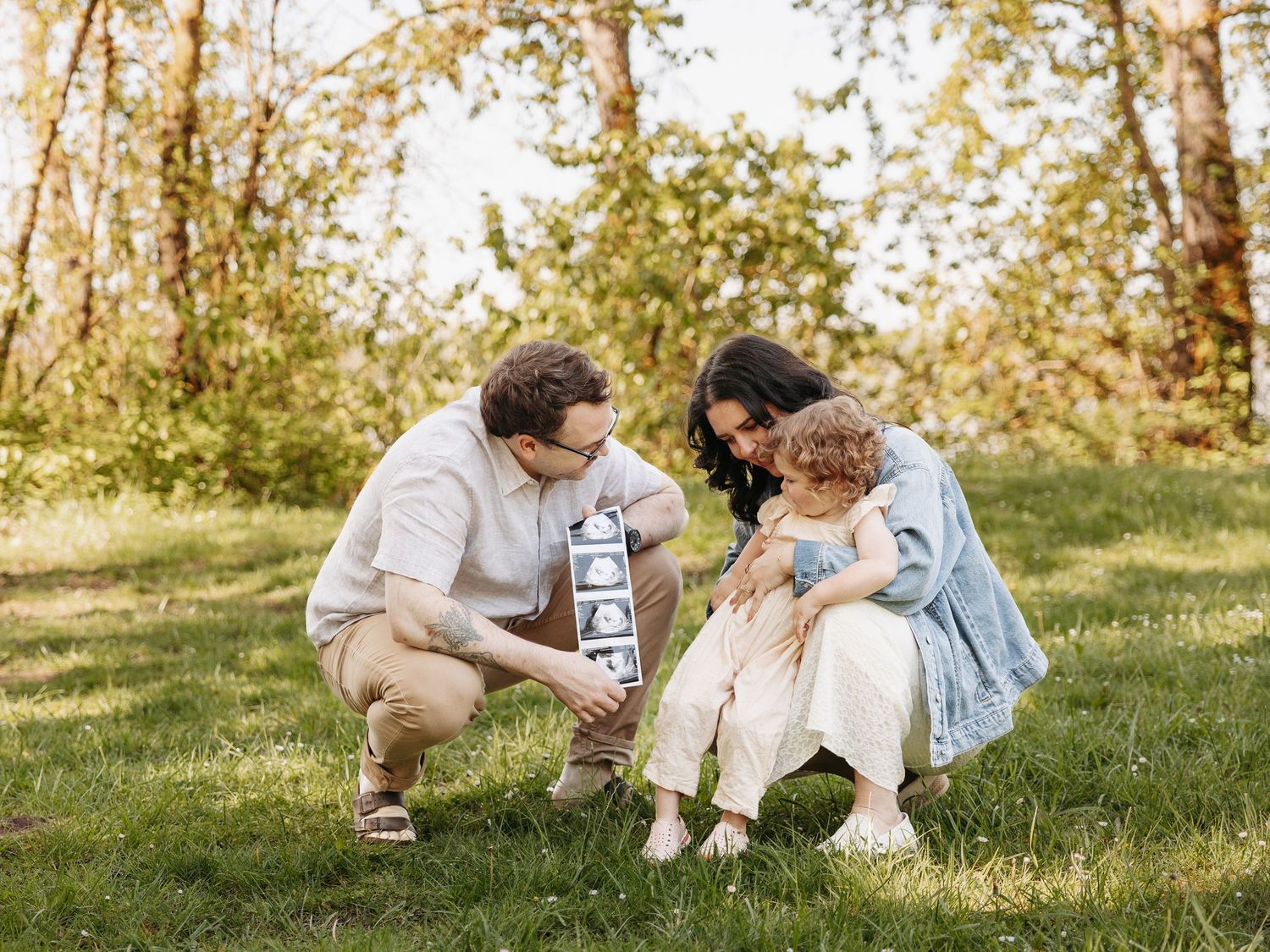 Family maternity session in outdoor setting near Portland Oregon, parents kneeling with toddler holding ultrasound photos
