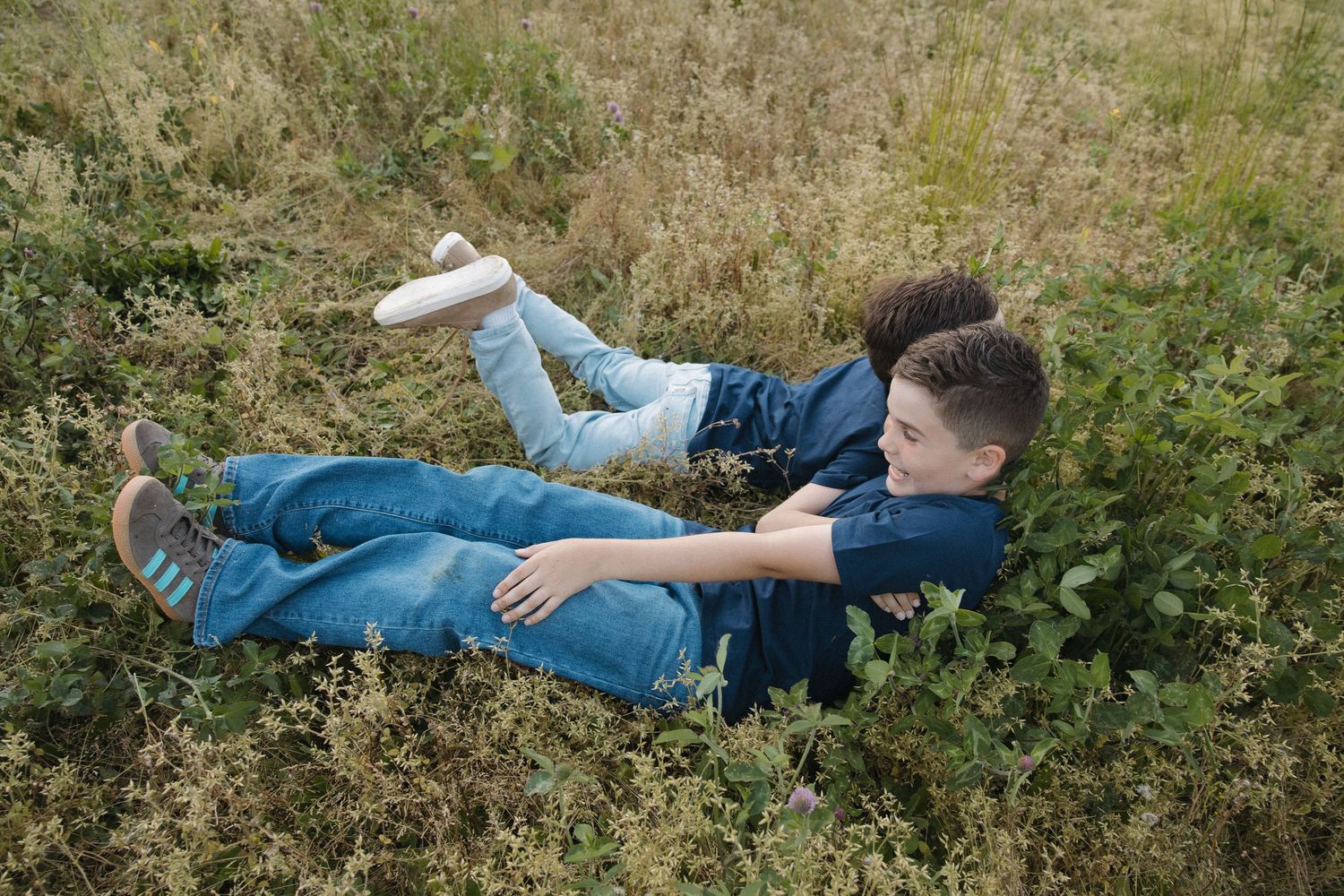 Two children playing and laughing together while lying in a grassy field on a sunny day.