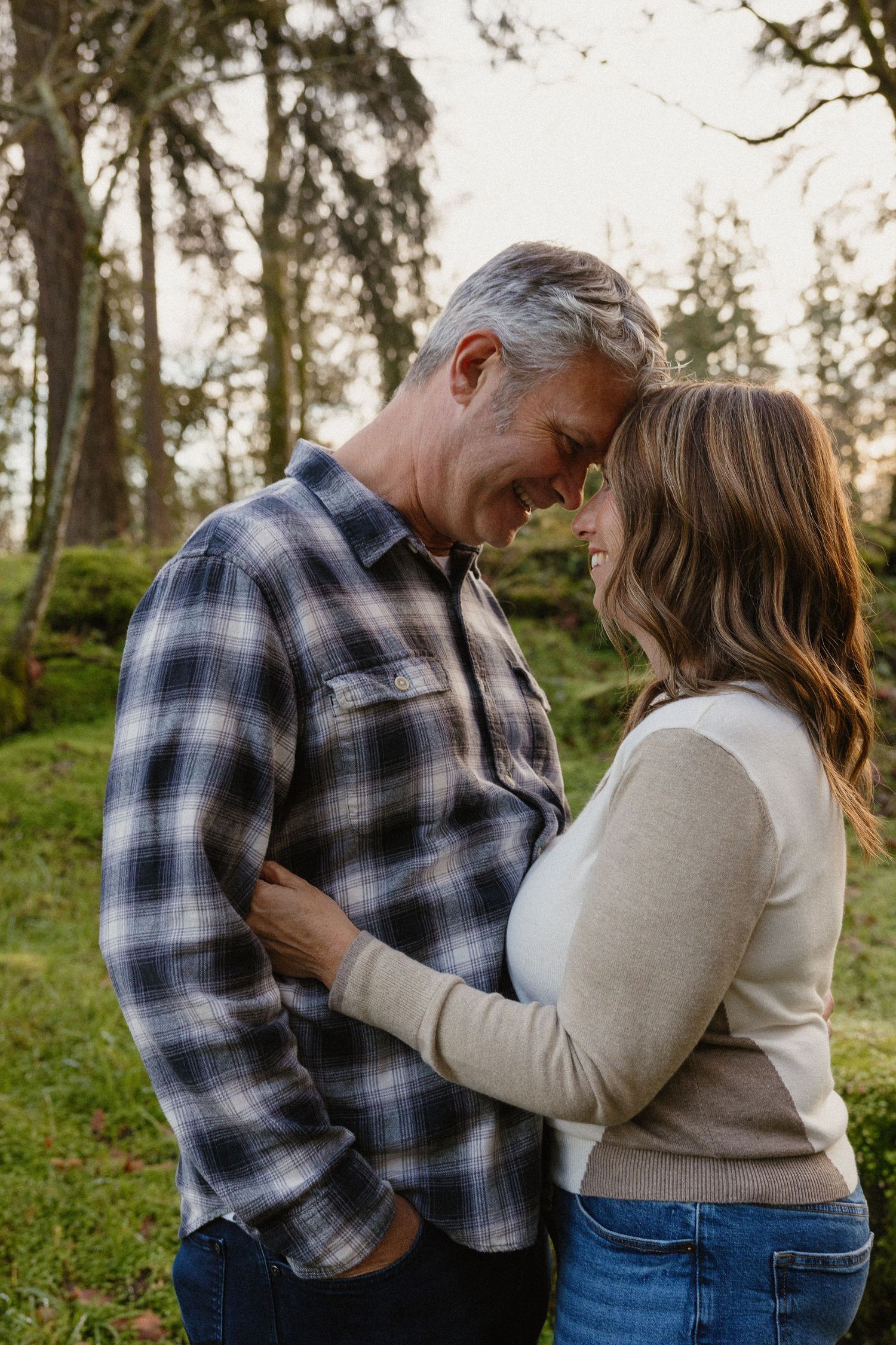 A couple shares a tender forehead-to-forehead moment in a lush green forest setting.