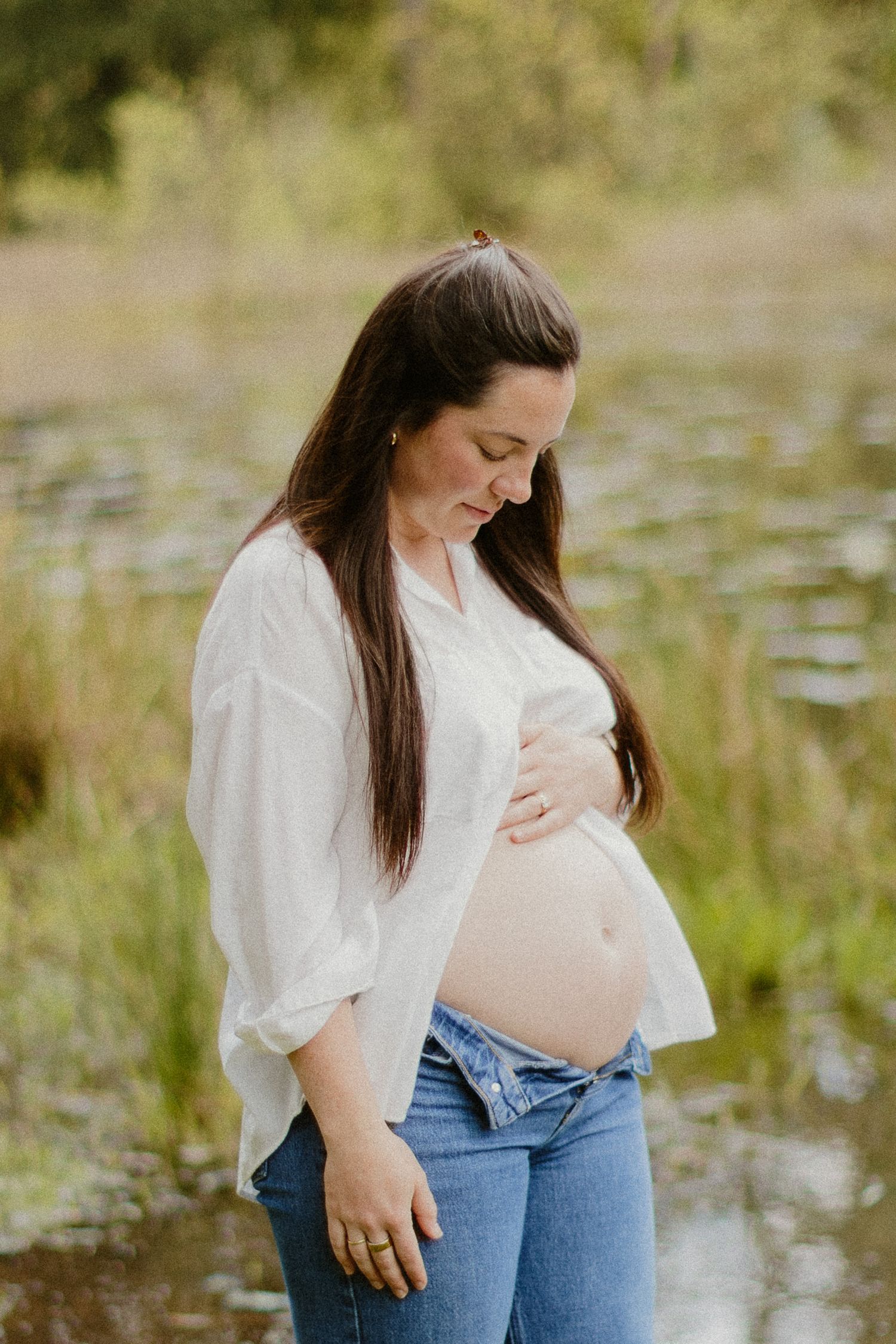 Pregnant woman cradling her baby bump by a serene pond.