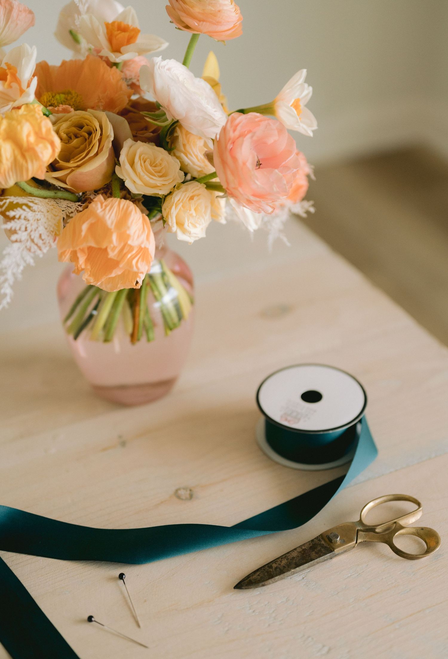 Peach-colored roses in a vase with black ribbon and scissors on a white marble surface create an elegant composition.