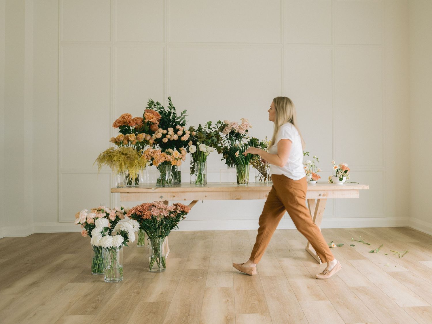 A florist arranges fresh floral displays on floating shelves in a minimalist white room with wooden floors.