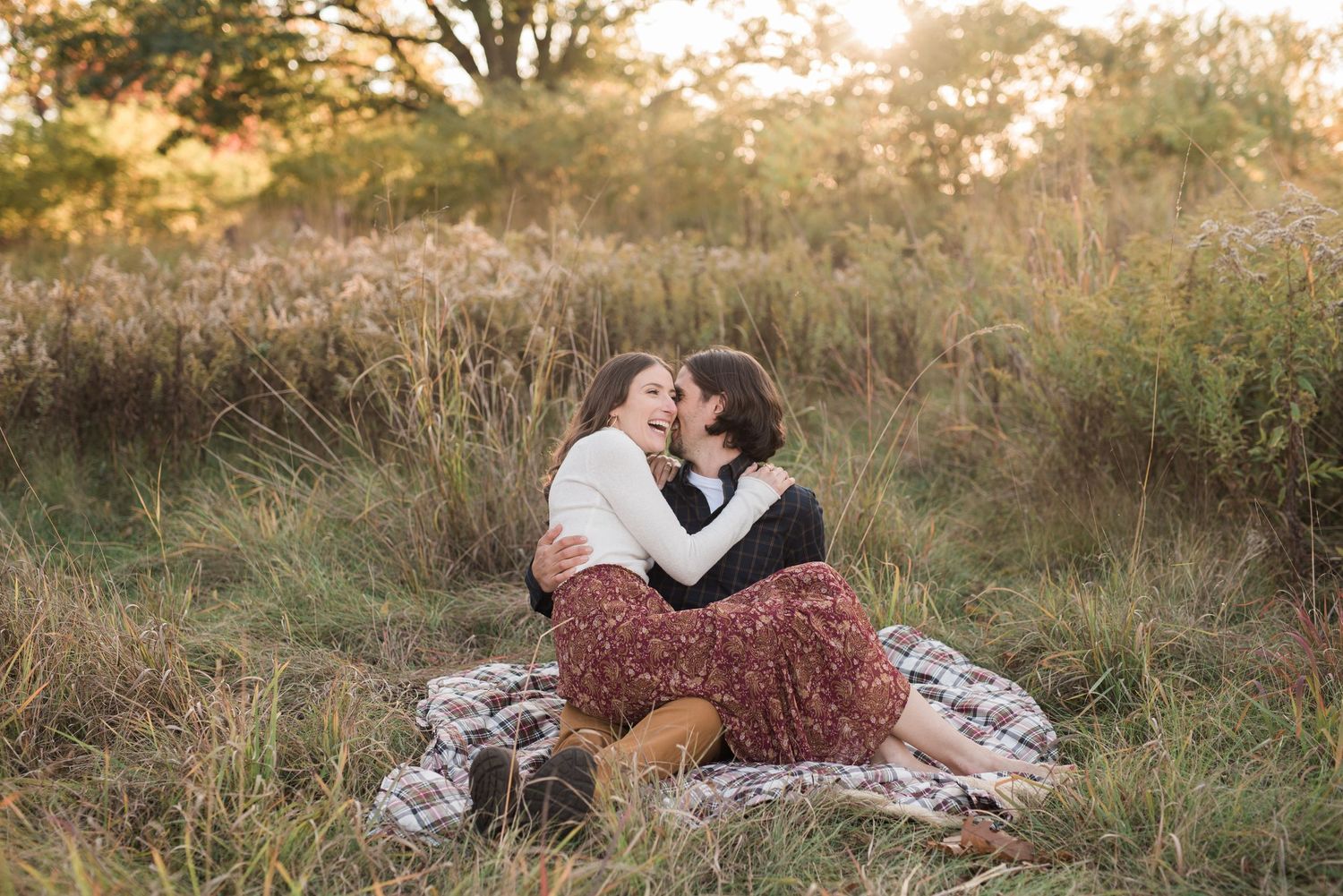 A couple shares an intimate moment together in a golden sunset-lit meadow with tall grass and natural lighting.