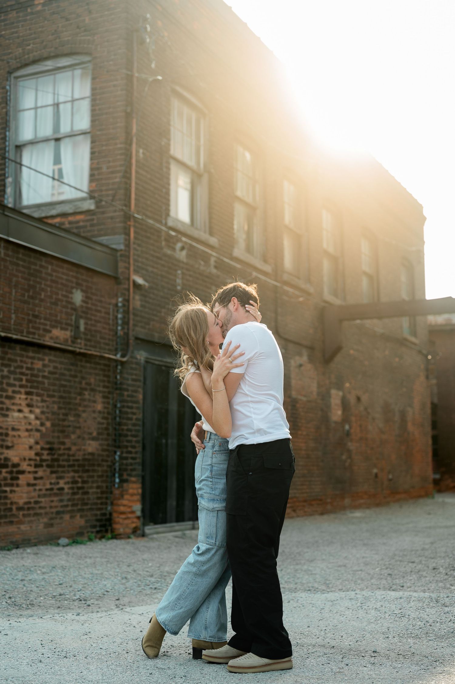 A couple embraces in front of a brick building during golden hour sunset.