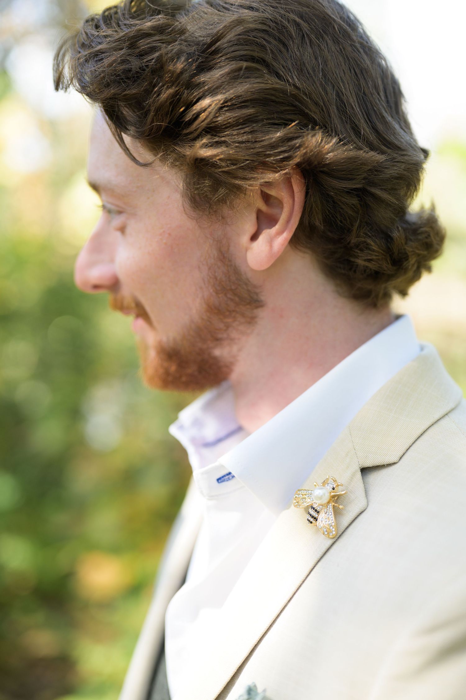 A groom in a light colored suit jacket shown in a series of close-up profile shots outdoors.