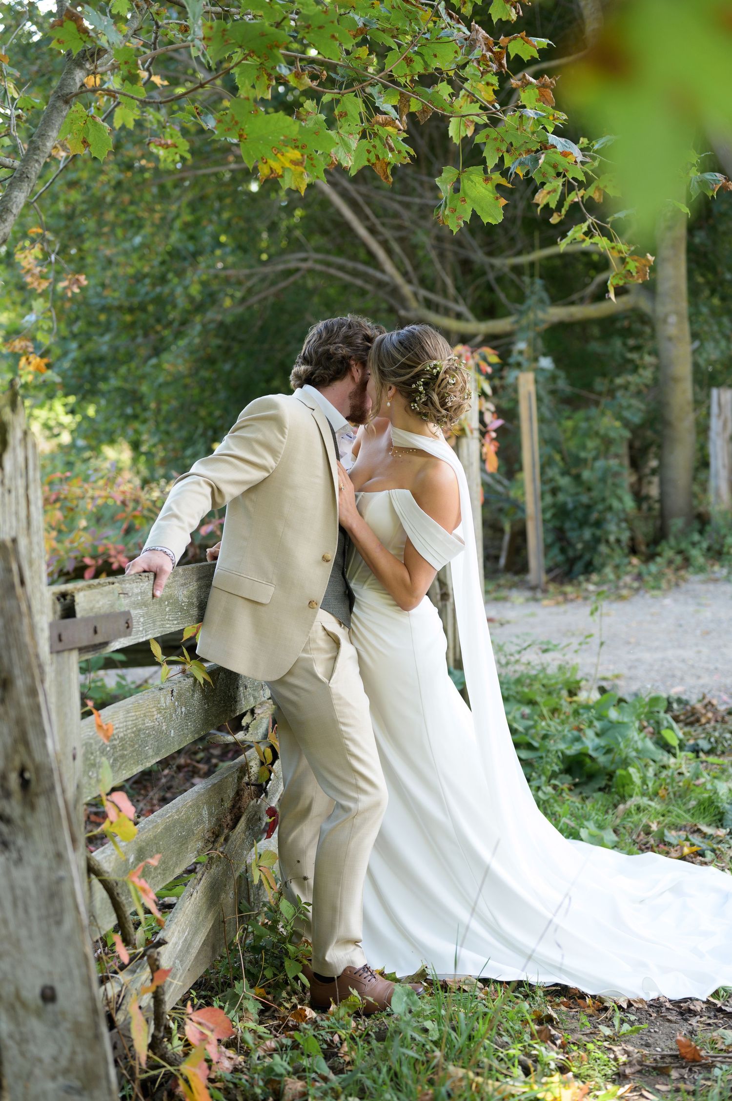 Romantic couple in wedding attire share intimate moments in a lush garden setting with autumn leaves.