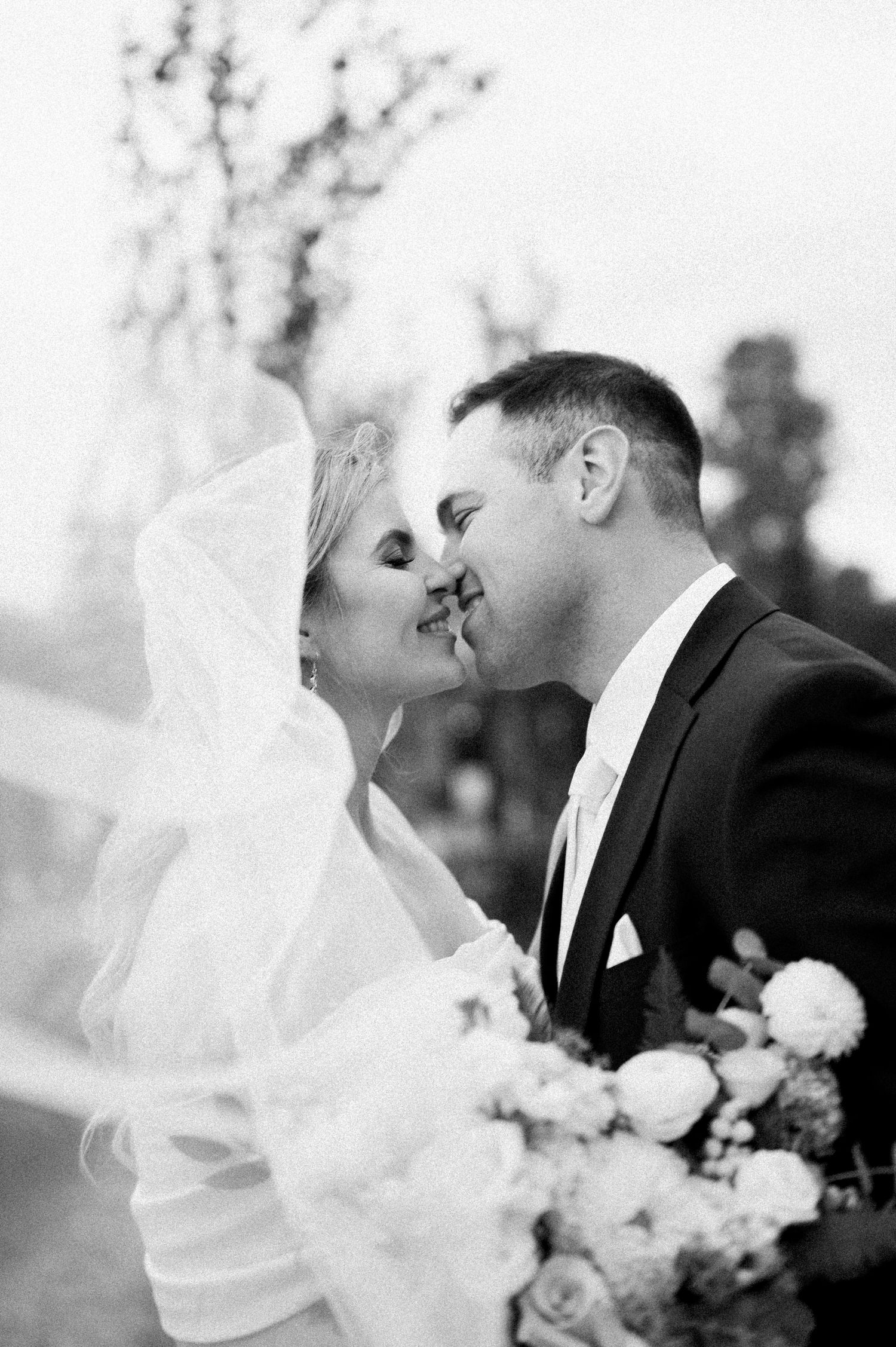 A romantic black and white wedding photo series showing a couple sharing tender kisses with floral bouquet details.
