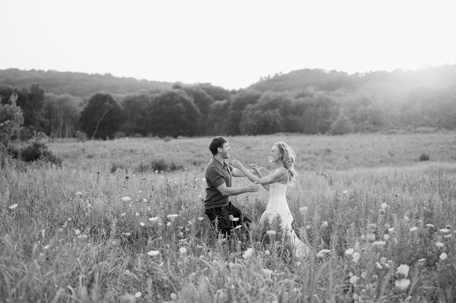 People walk through a sunny meadow filled with wildflowers and tall grass on a summer afternoon.