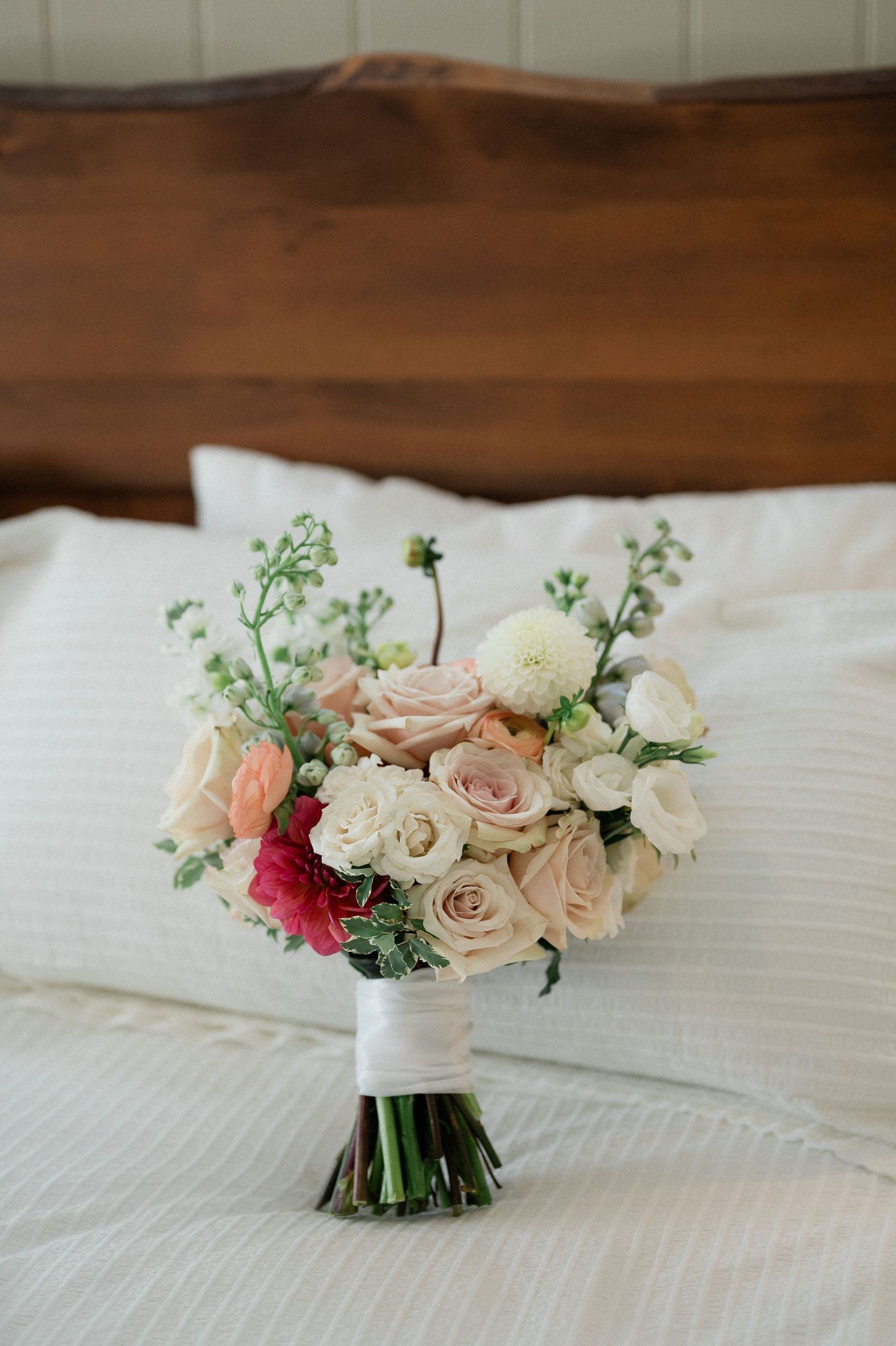 A delicate wedding bouquet with blush pink roses, white flowers and eucalyptus greenery rests on white linens.