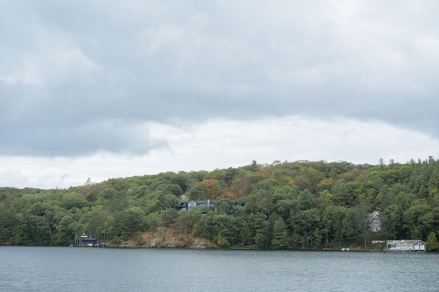 Panoramic view of a wooded coastline with buildings nestled along the waterfront and green hills in the background.