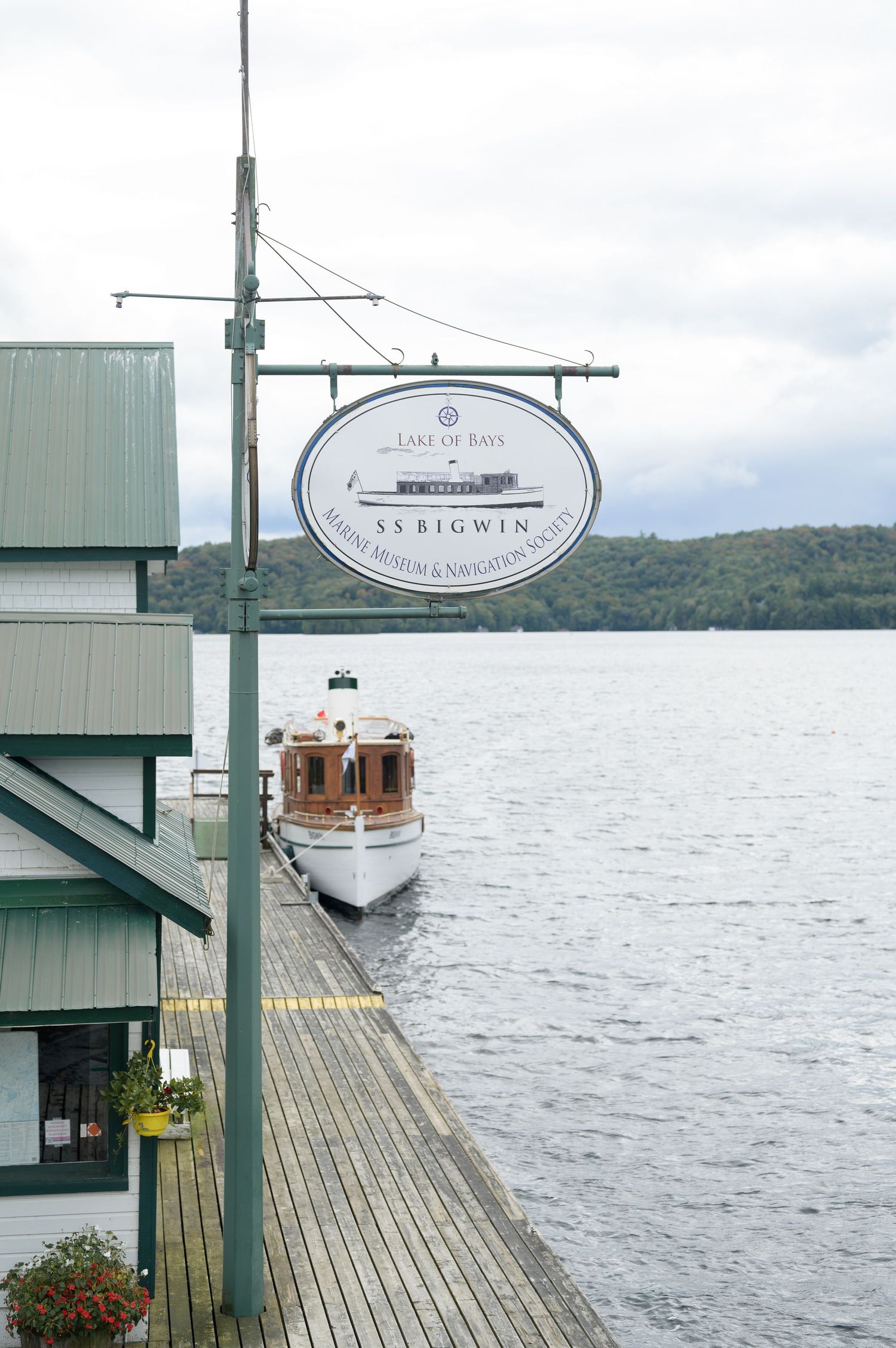 A vintage wooden boat docked at a lakeside pier with a hanging business sign and scenic water views.