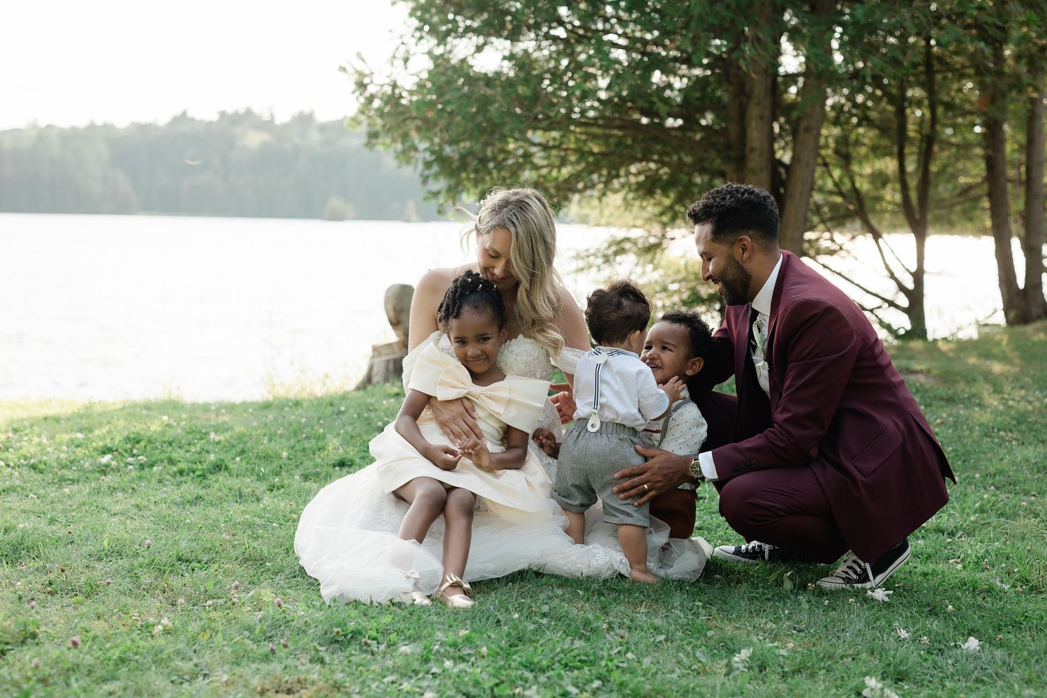 Family in formal attire sits together on grass by lakeside during outdoor photo session.