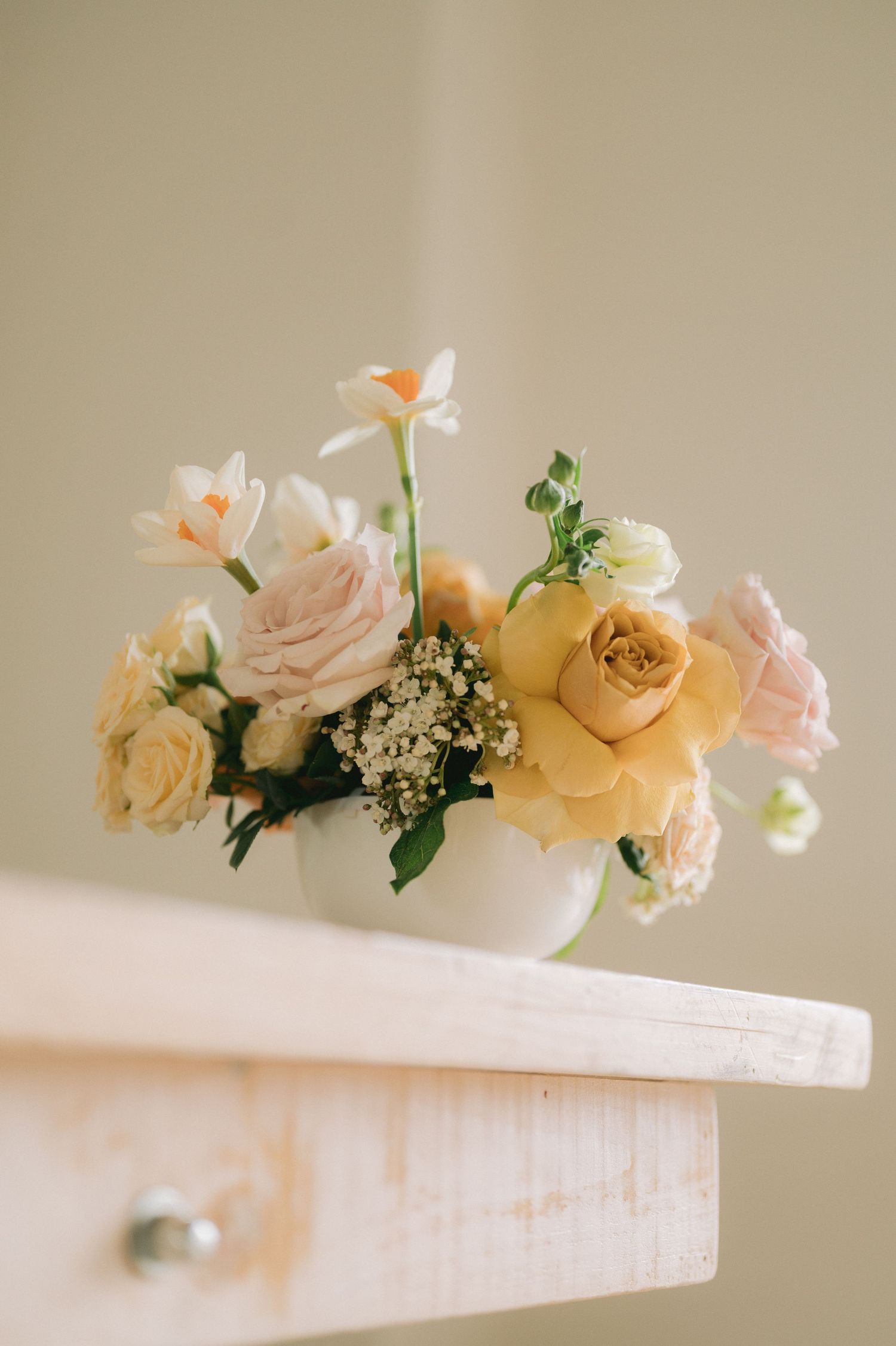 Delicate floral arrangement featuring peach roses and white flowers displayed on a light wooden surface.