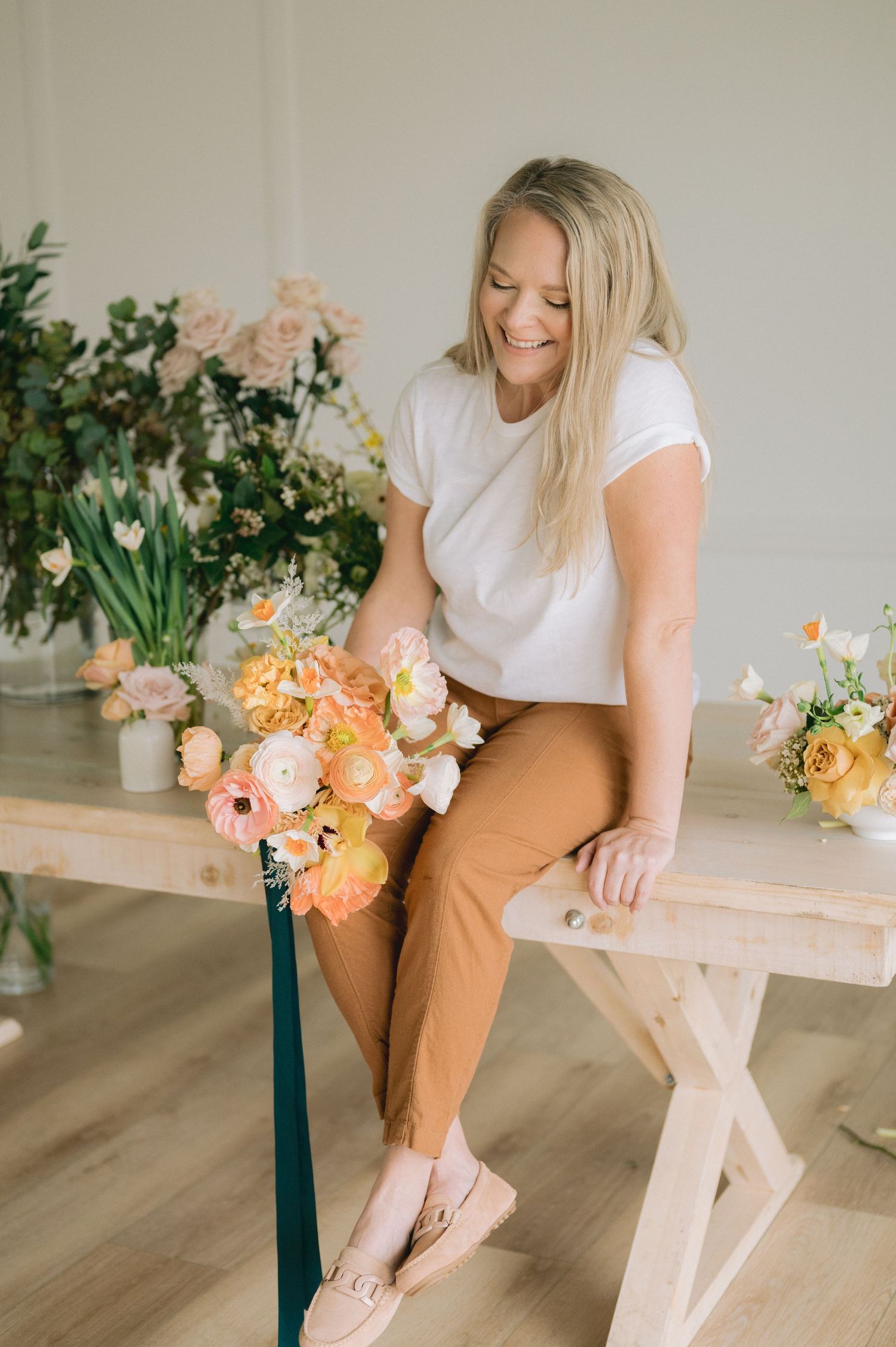 Person in casual attire sitting on wooden bench with floral arrangements in soft peach and coral tones.