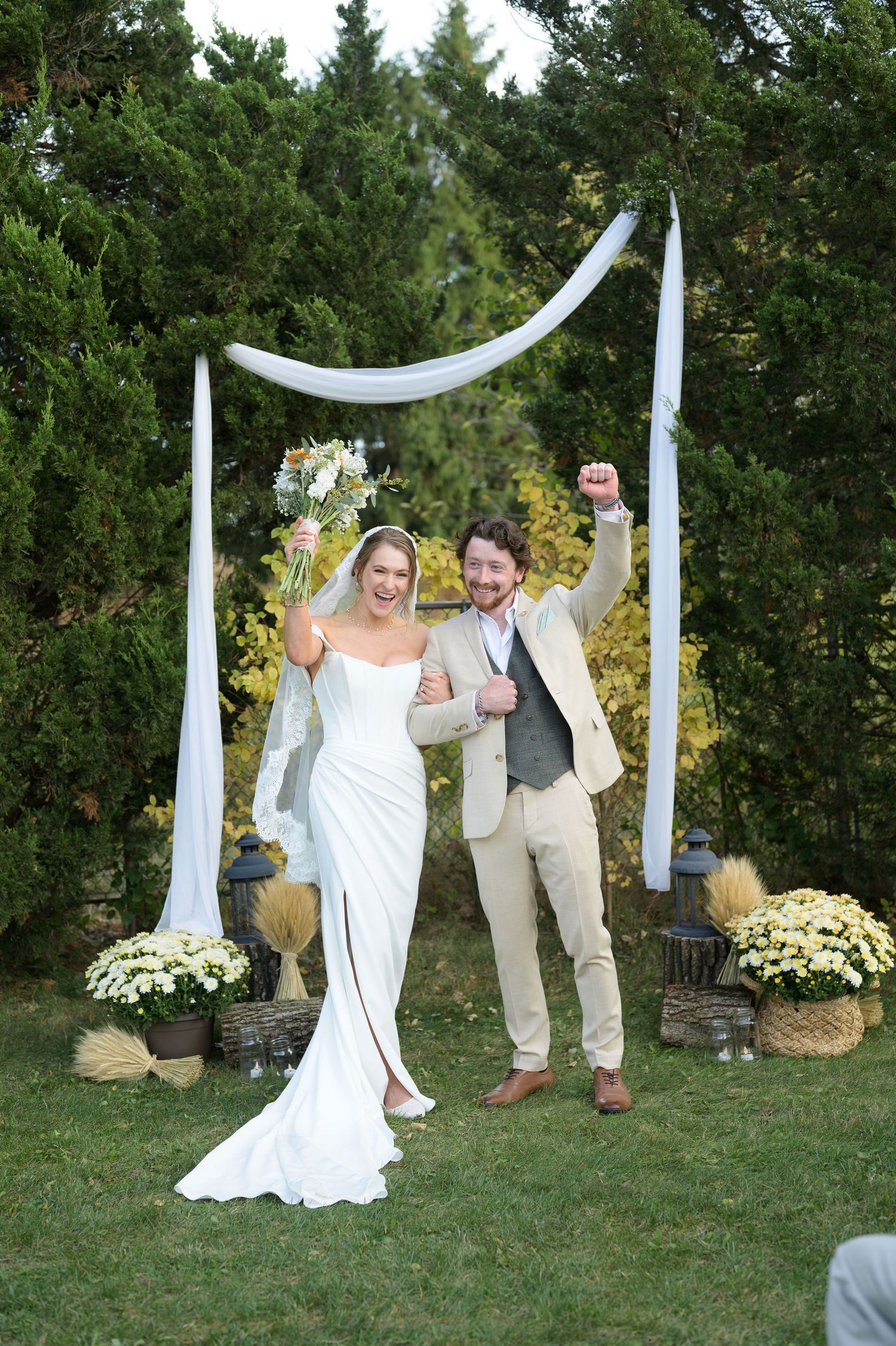 Outdoor wedding ceremony setup with white fabric draping and yellow floral arrangements against green trees.