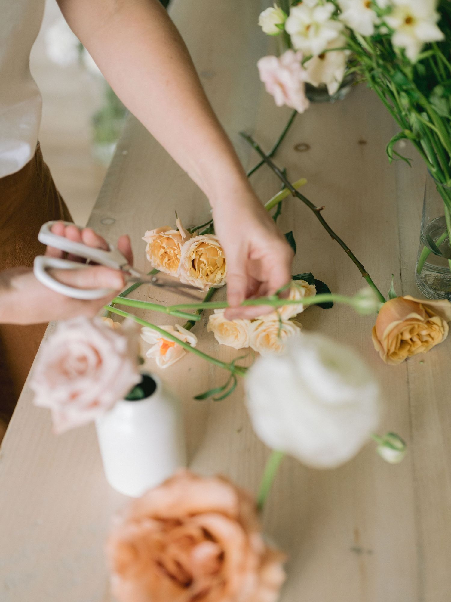 Close-up shots of hands arranging delicate peach and white flowers in ceramic vases.