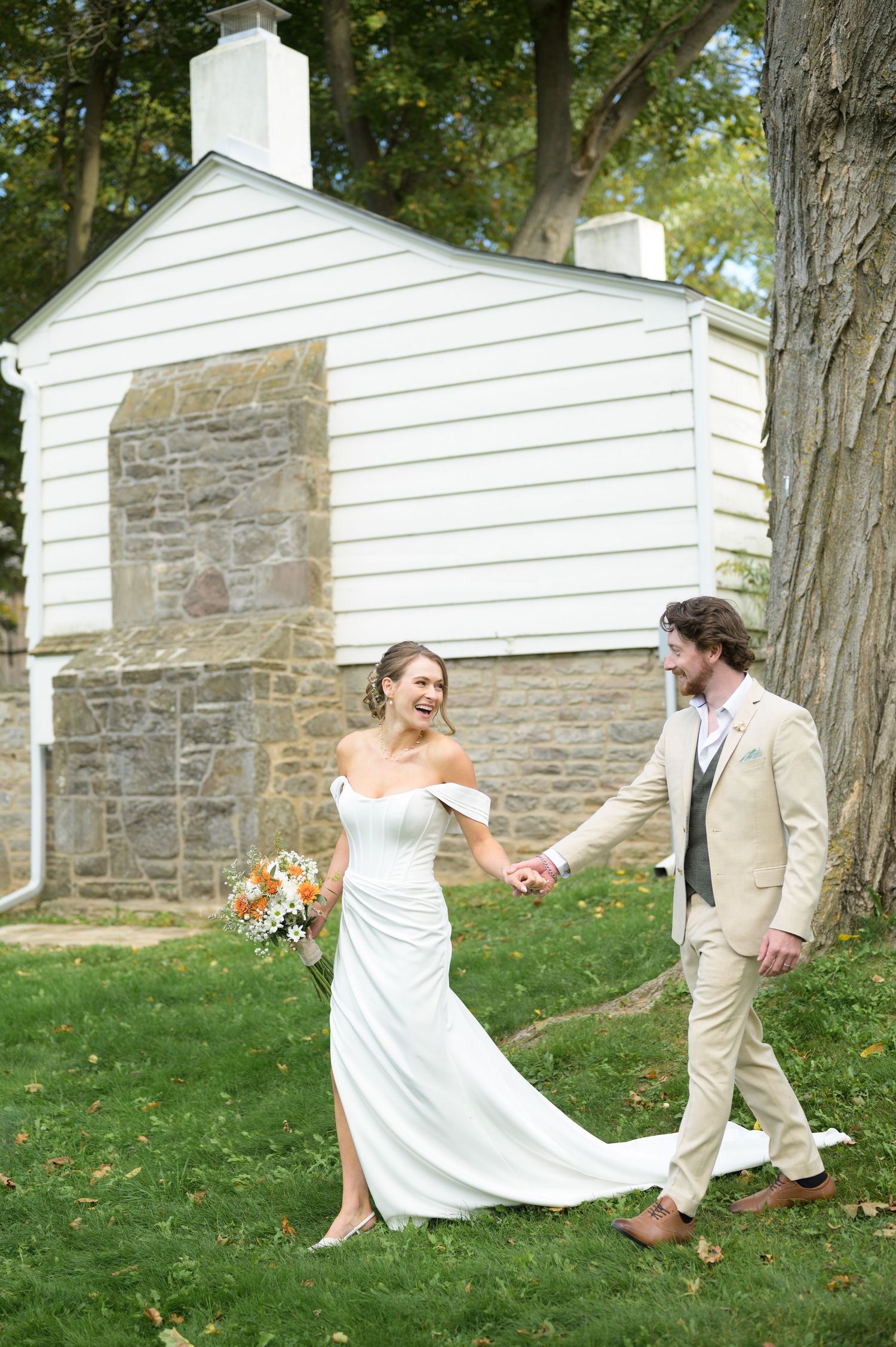 A couple dances playfully on a grassy hillside near white stone buildings.