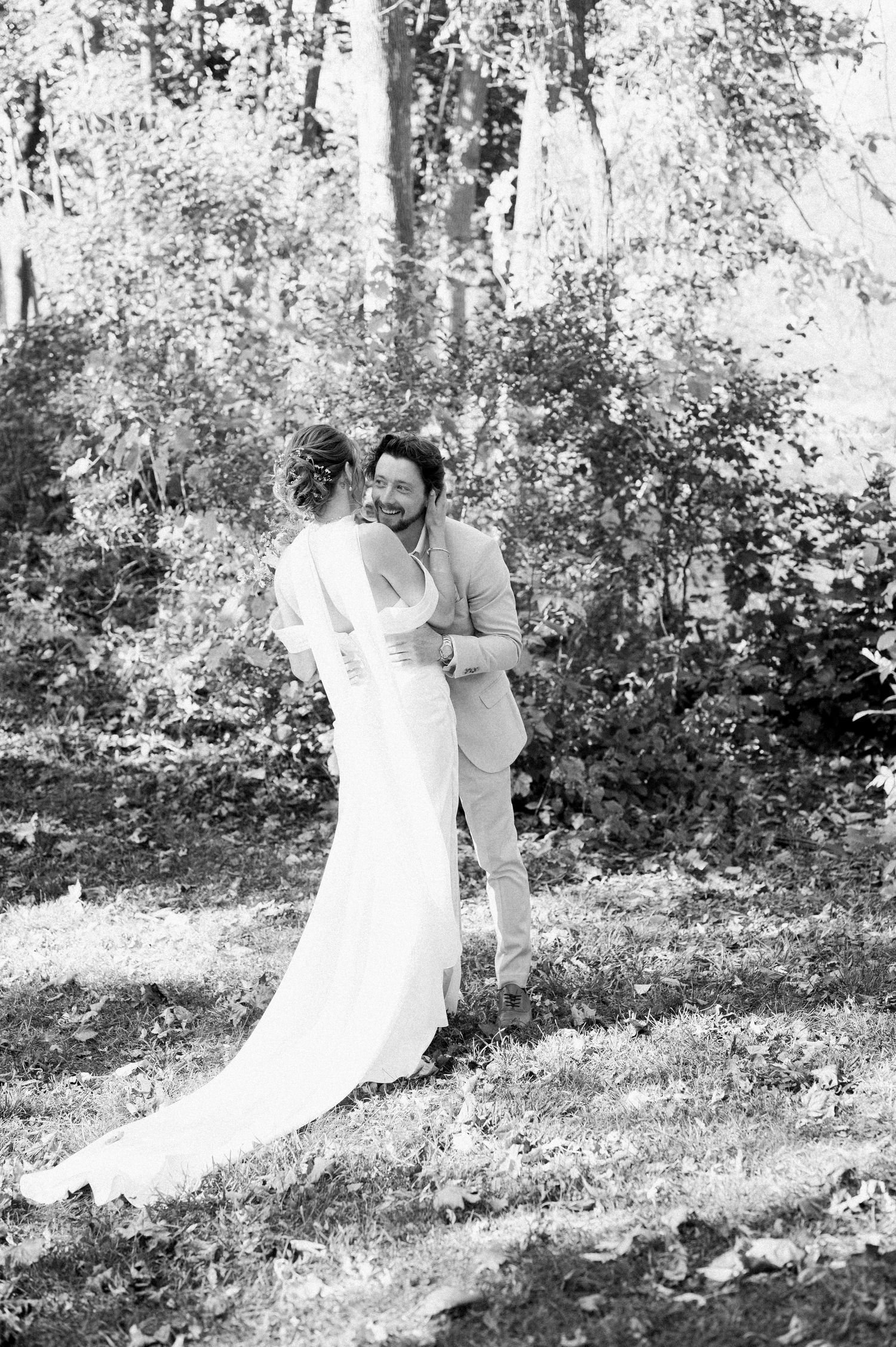 Black and white photo of a tender wedding moment captured in a wooded outdoor setting.