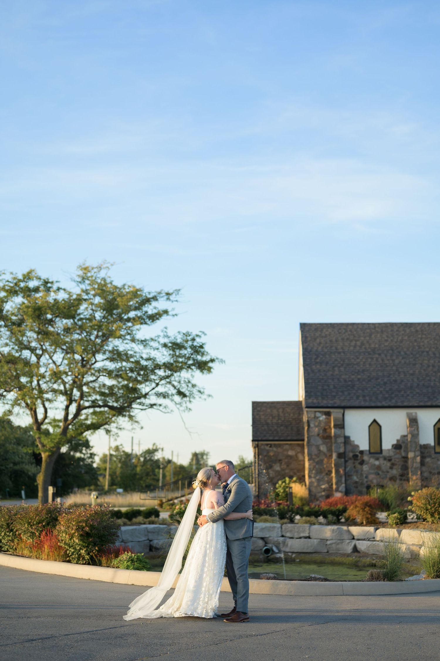 A couple shares romantic moments at sunset outside a rustic stone church with autumn foliage in the background.