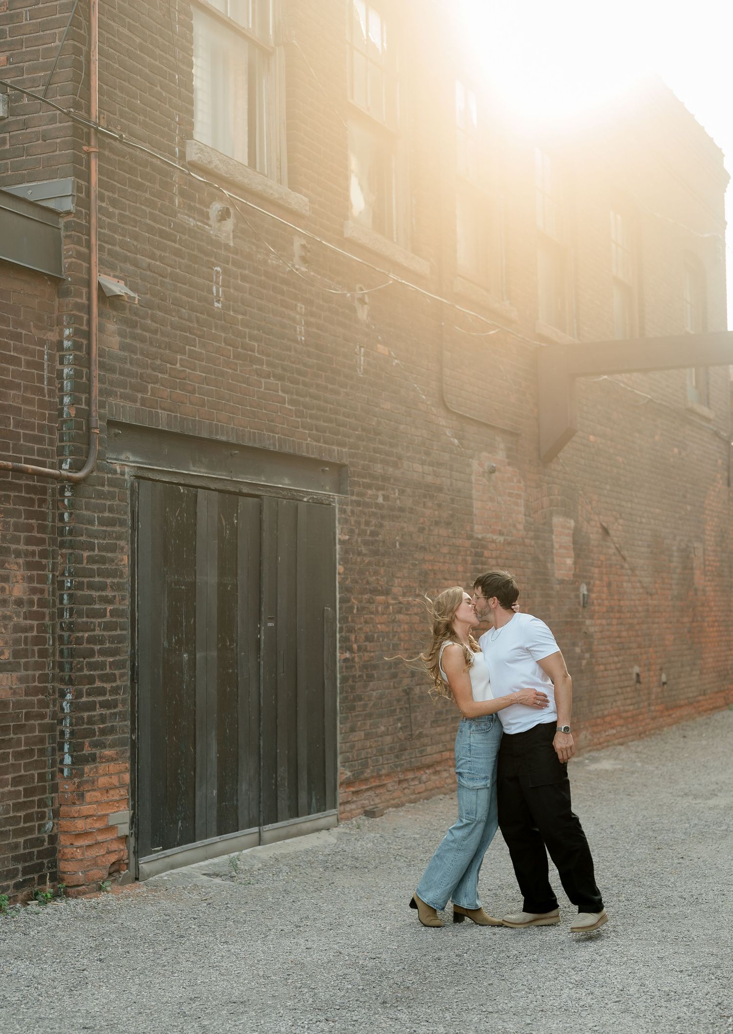 Romantic proposal scene at sunset against a rustic brick building backdrop.